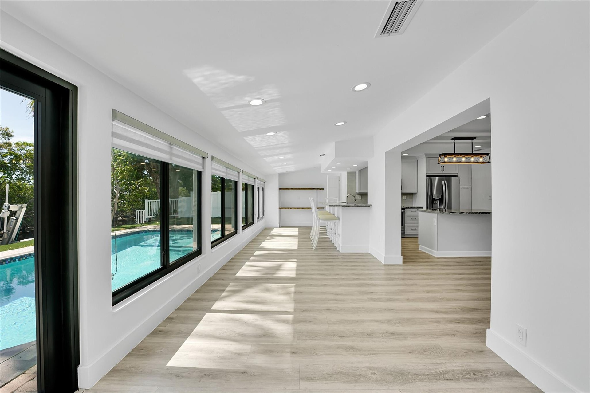 Bright interior with wood-finish flooring, recessed lighting, expansive windows overlooking a pool, and an open-concept kitchen featuring an island wi
