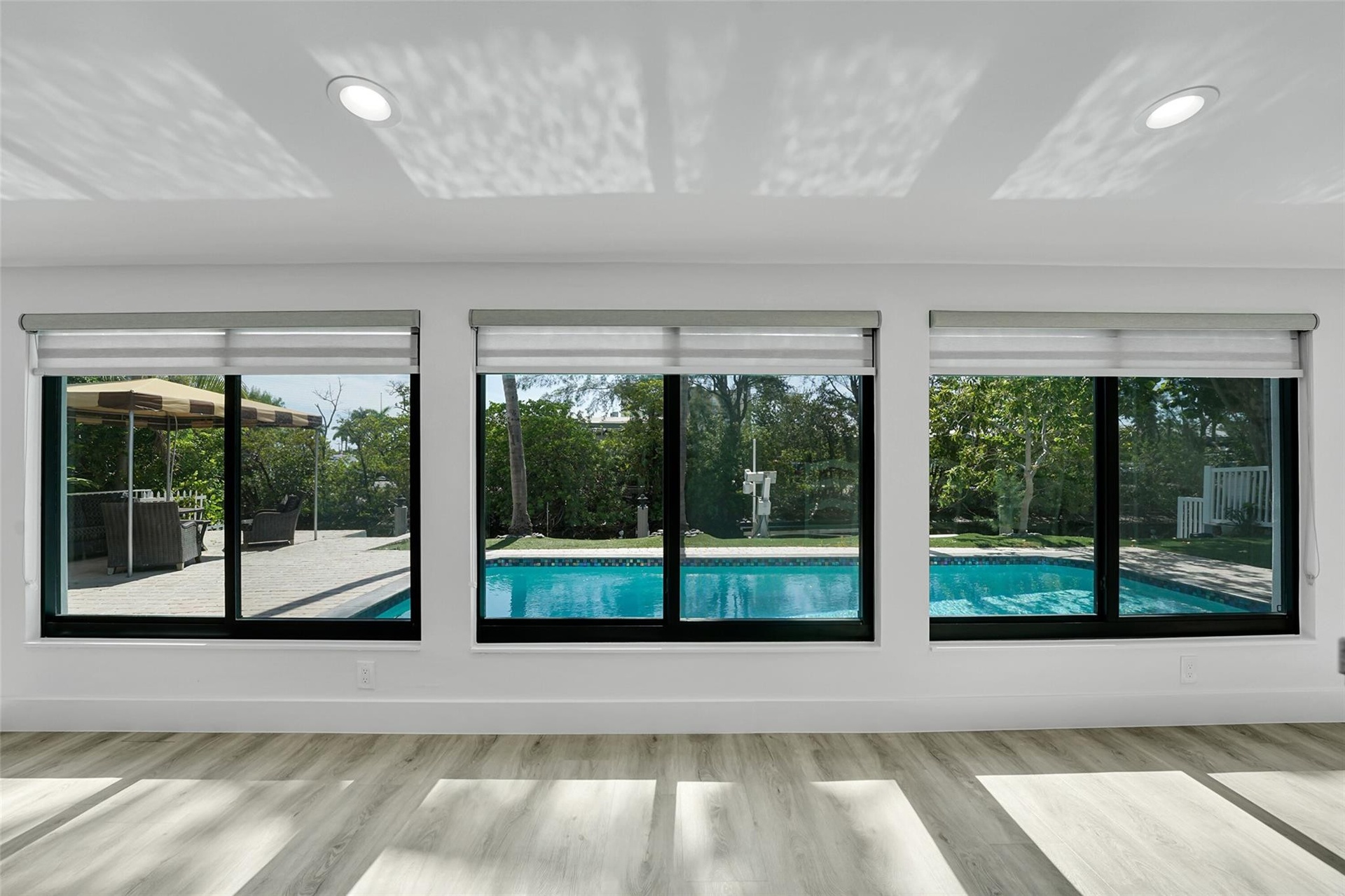 Light wood-finish flooring, recessed ceiling lighting, roller shades, and a swimming pool