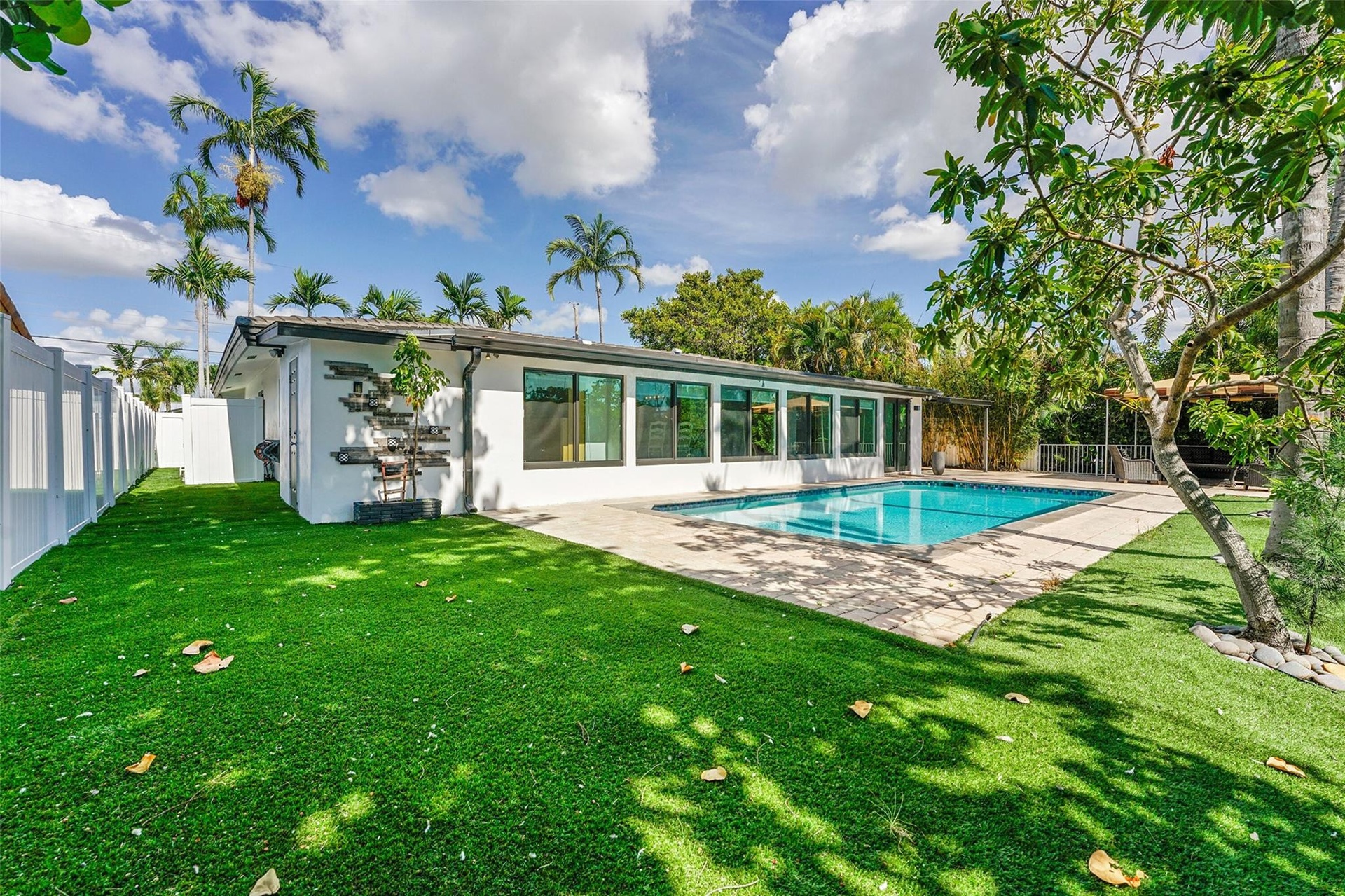 Expansive backyard featuring a rectangular swimming pool, paver deck, artificial turf, and privacy fencing