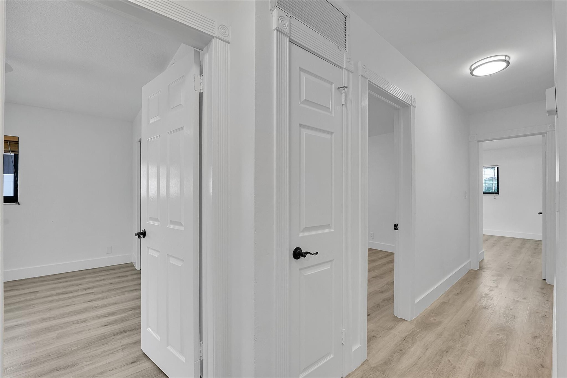 Wood-finish flooring throughout, bright white walls, and contemporary flush-mount lighting fixtures