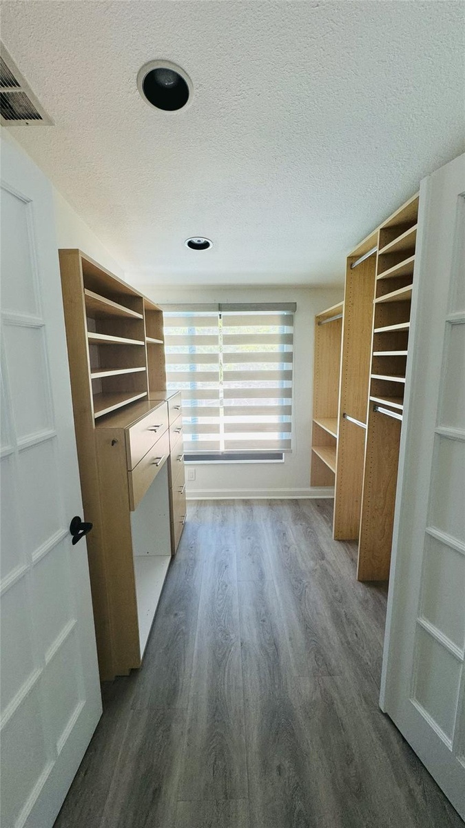 Walk-in closet with custom built-in shelving, drawers, wood-finish flooring, and recessed lighting