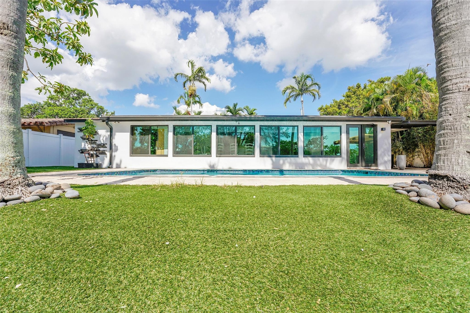 Expansive artificial turf lawn with a large swimming pool, surrounded by a white exterior and extensive tinted windows