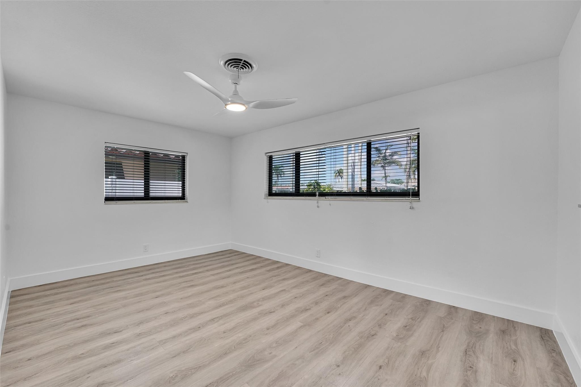Wood-finish flooring with white baseboards, white walls, and a modern ceiling fan
