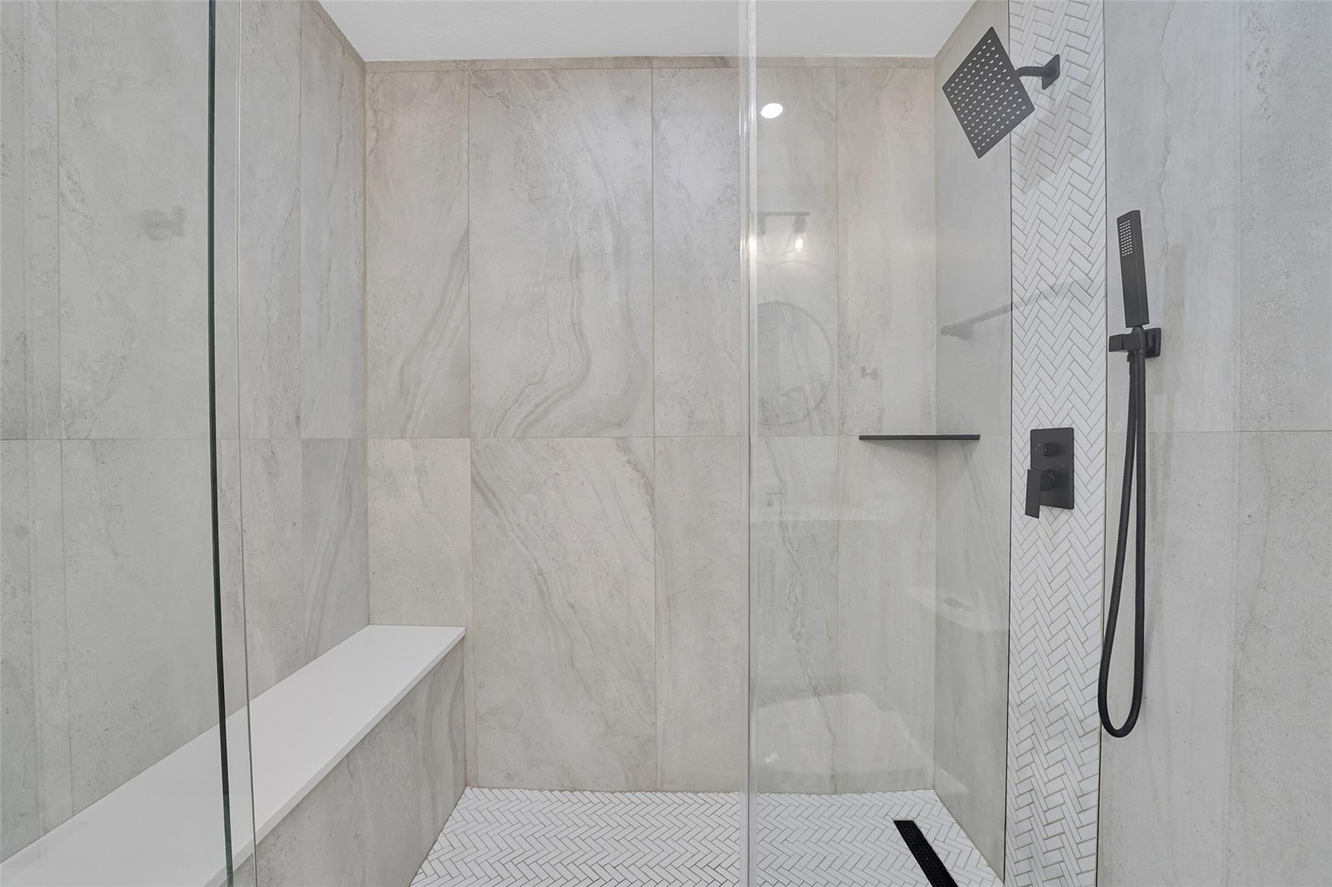 Walk-in shower featuring a built-in bench, glass enclosure, matte black fixtures, and herringbone-patterned floor tile