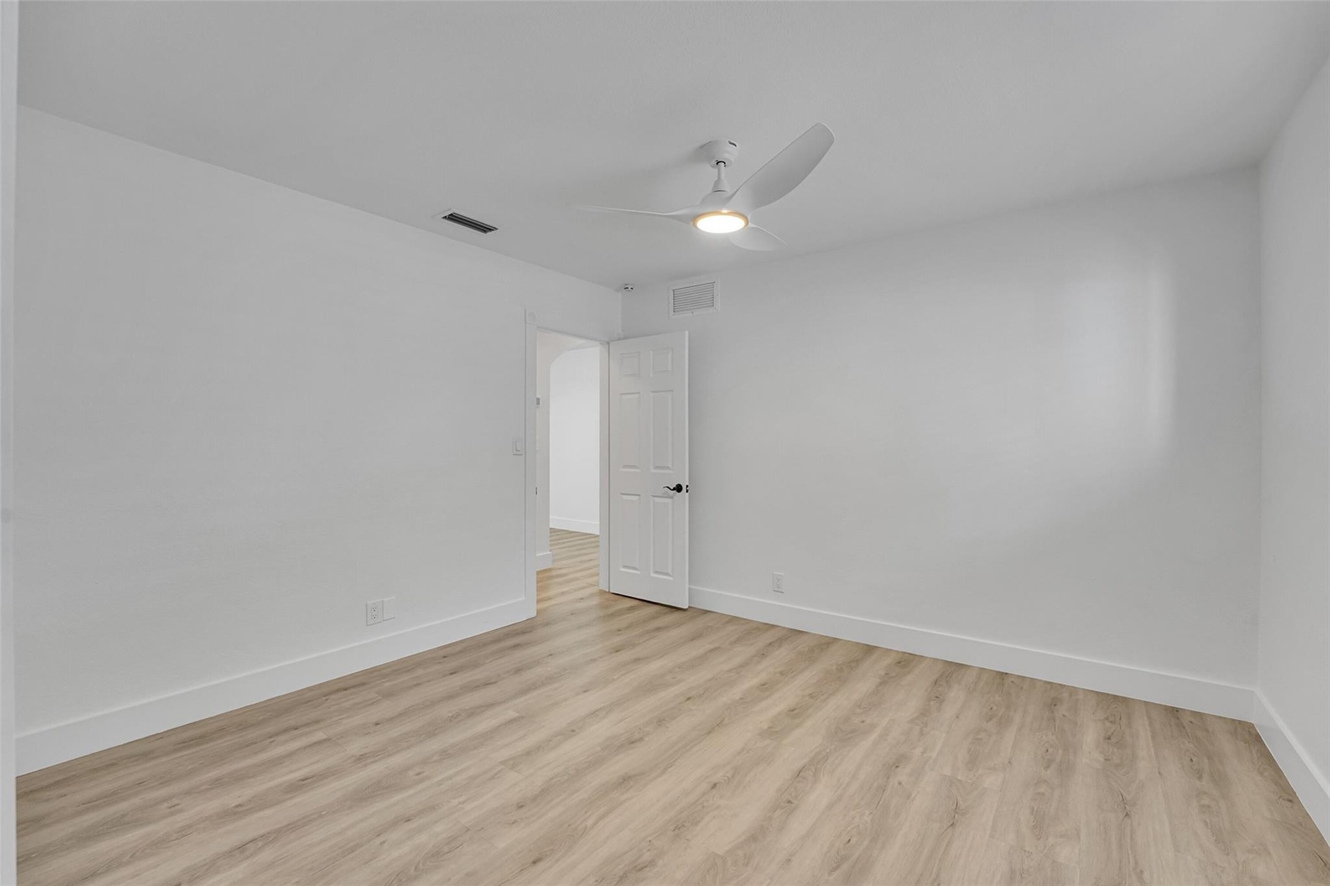 Wood-finish flooring, white walls, white ceiling fan with integrated lighting, and a white paneled door