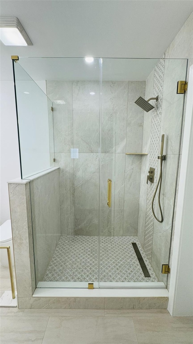 Glass-enclosed shower featuring a rain shower head, hand-held shower, tiled walls, a built-in shelf, and a patterned tile floor