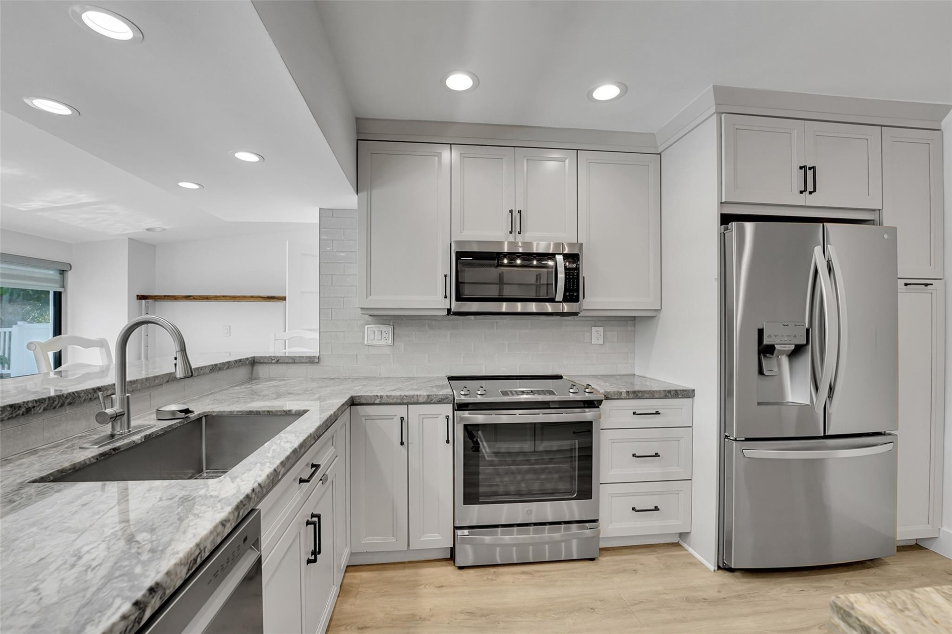 Well-appointed kitchen featuring light-toned cabinetry, stainless steel appliances, a subway tile backsplash, recessed lighting, and wood-finish floor