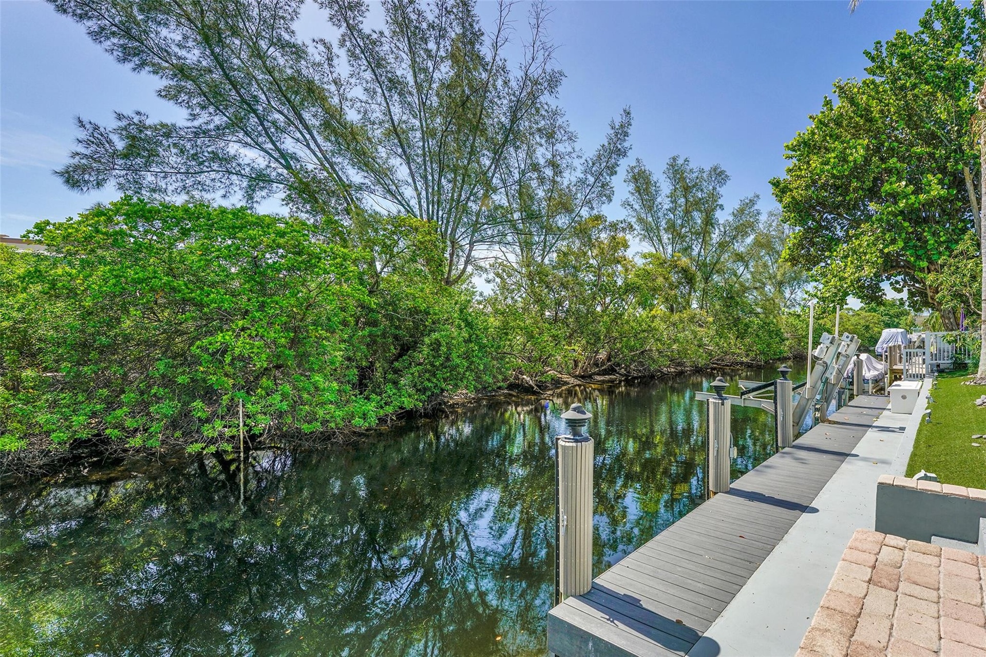 Waterfront property featuring a private boat dock, lush mature trees, and a paver patio