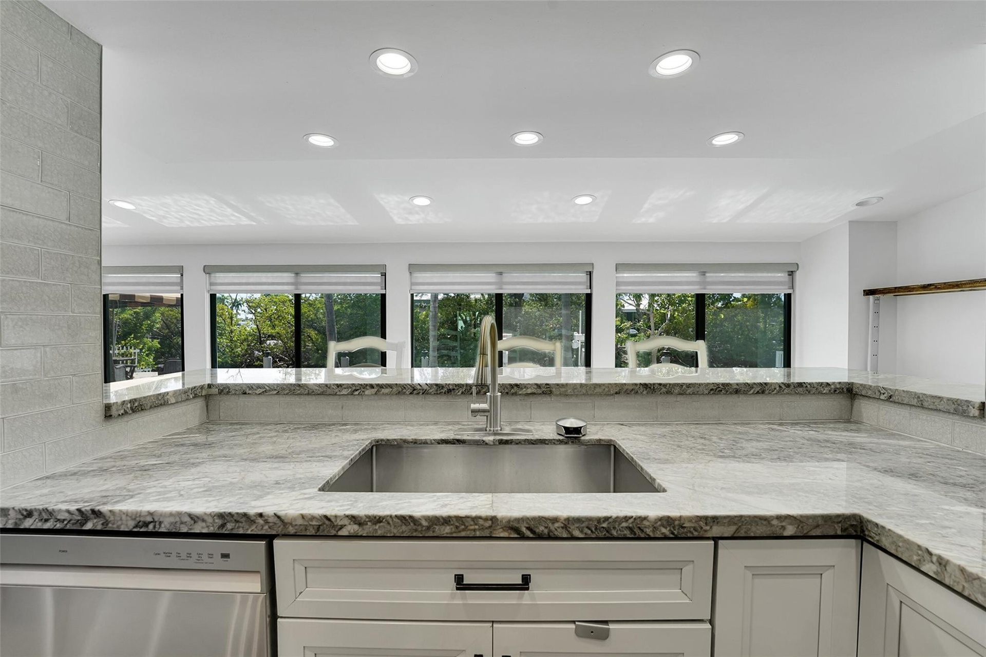 Kitchen featuring white shaker cabinetry, stainless steel sink, gold-finish faucet, and light-toned stone countertops