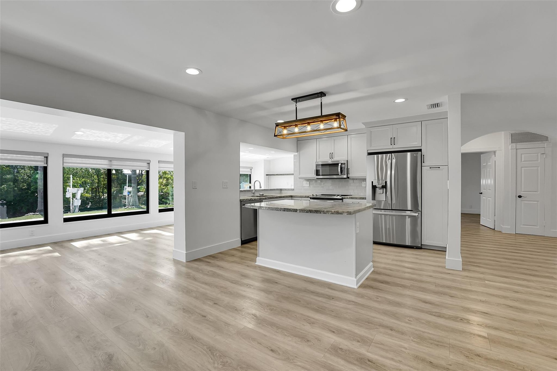 Open-concept living space with wood-finish flooring, recessed lighting, and a kitchen island featuring a stone countertop
