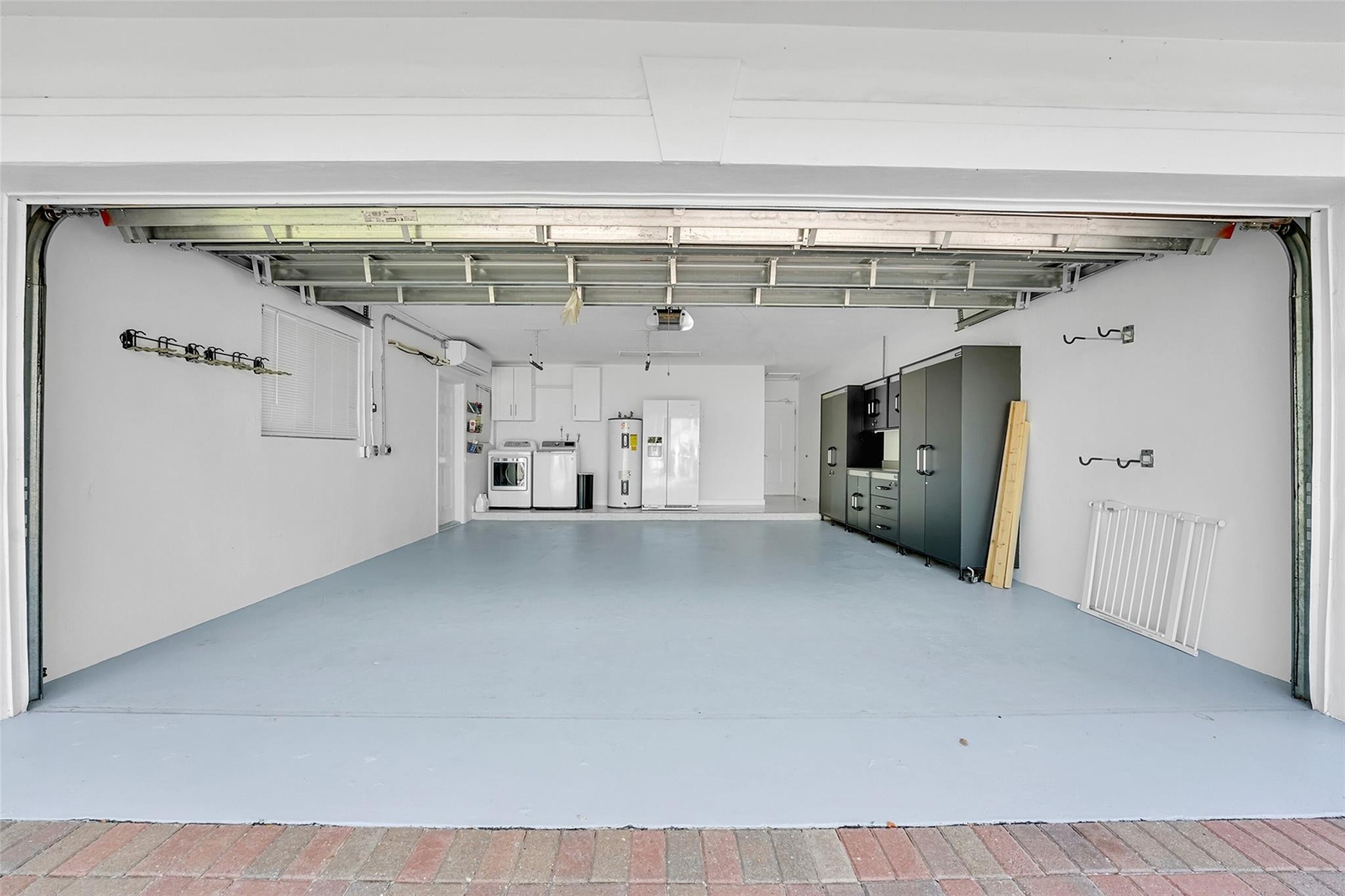 Expansive garage with light-toned flooring, built-in cabinetry, overhead structural elements, and a wall-mounted window