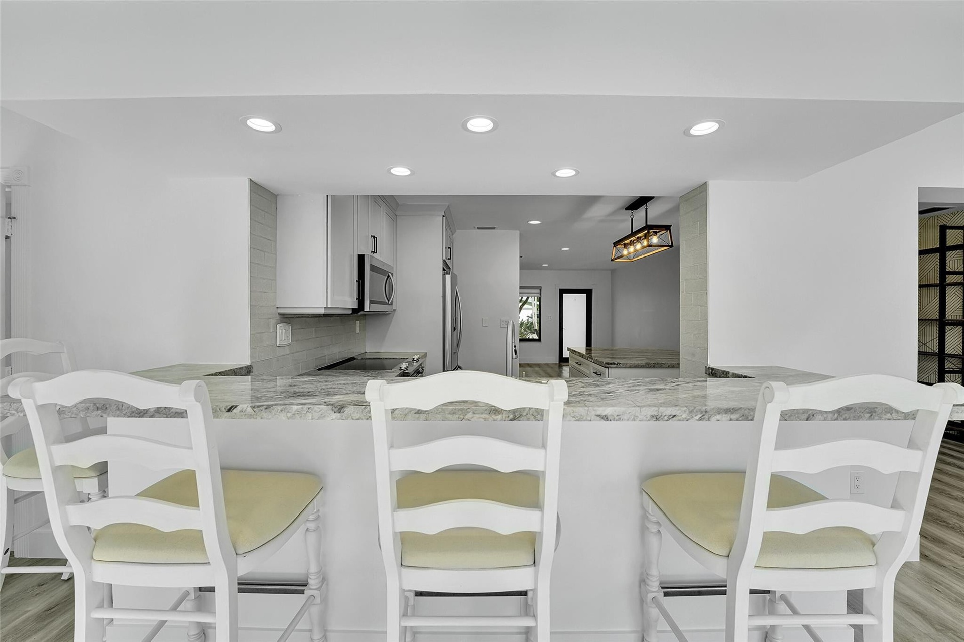 Kitchen featuring a breakfast bar with stone-finish countertop, recessed lighting, white cabinetry, stainless steel appliances, and a subway tile back