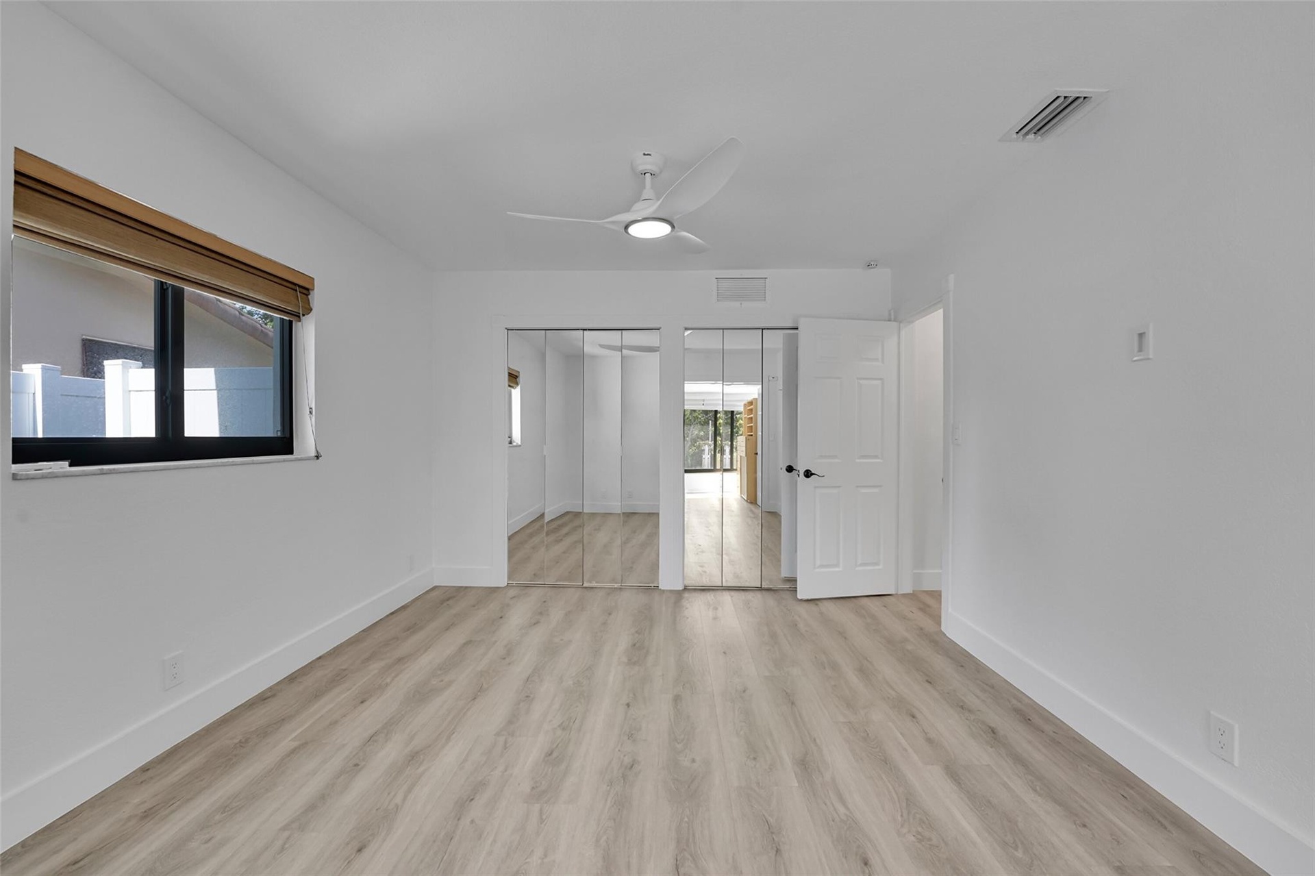Wood-finish flooring, mirrored closet doors, a contemporary ceiling fan, and a single window with blinds