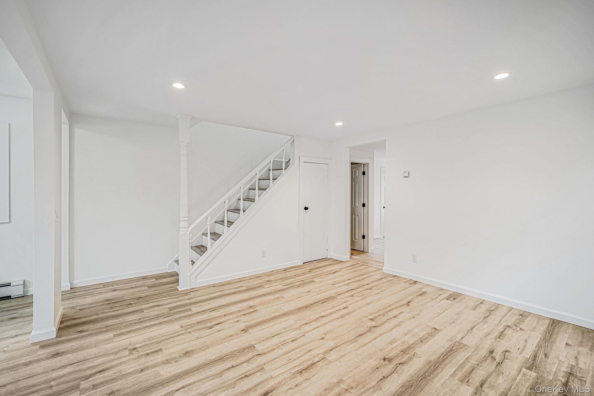 Open-concept interior featuring wood-finish flooring, recessed lighting, and a staircase with white balusters and a decorative post