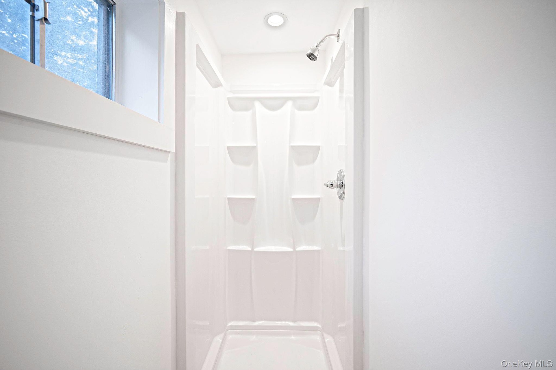 First floor shower enclosure featuring a high-gloss composite surround with integrated storage shelving, a wall-mounted showerhead, and a recessed cei
