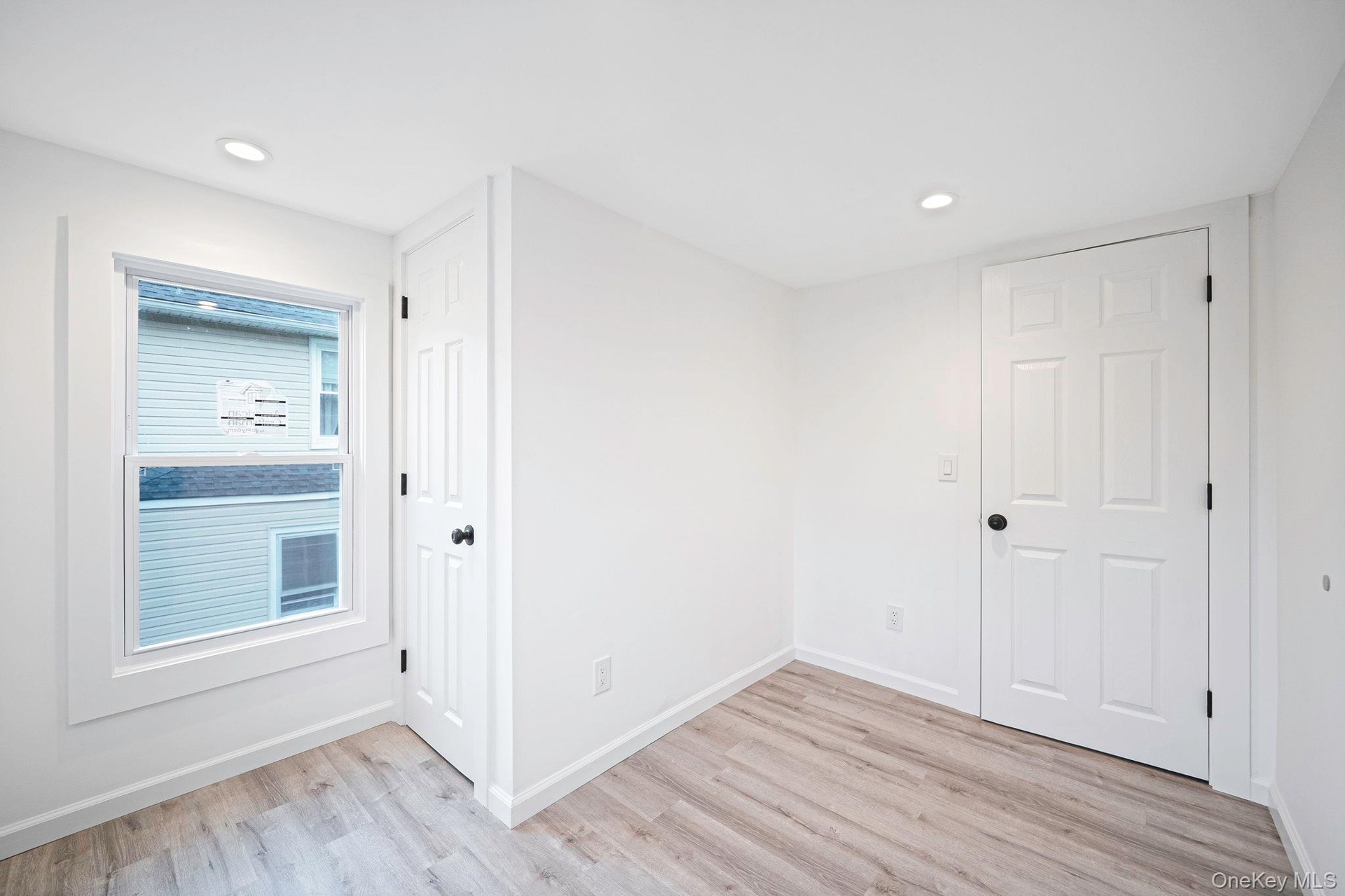 Neutral-toned interior space featuring vinyl wood-finish flooring, recessed lighting, white six-panel doors, and a double-hung window with wide casing