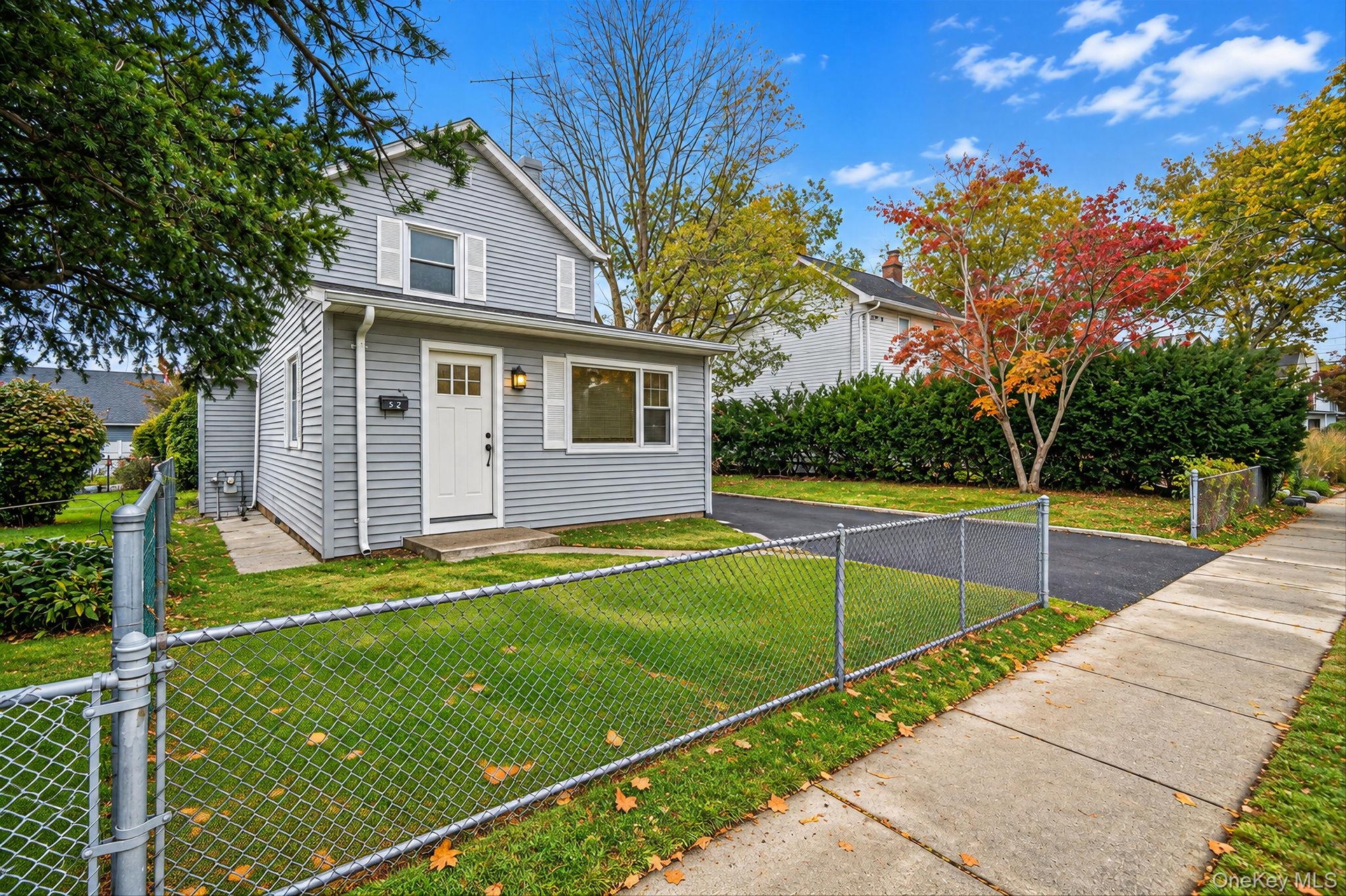 Two-story vinyl-sided exterior featuring white shutters, an asphalt driveway, and a chain-link fence *virtually edited