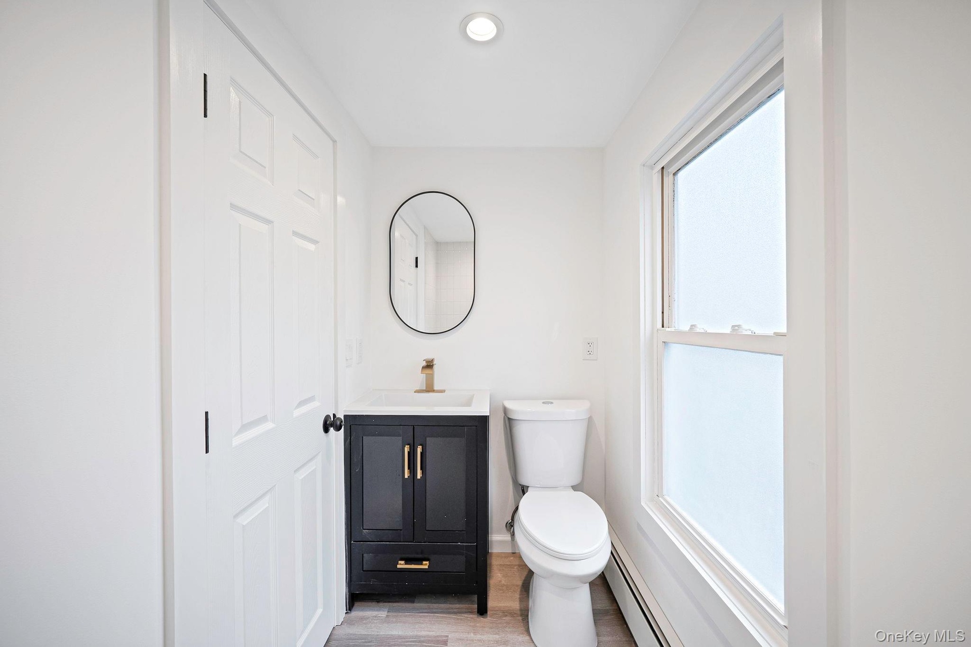 Second floor bathroom featuring dark-finished vanity with gold-tone hardware, rectangular undermount sink, oval wall-mounted mirror, and wood-finish f