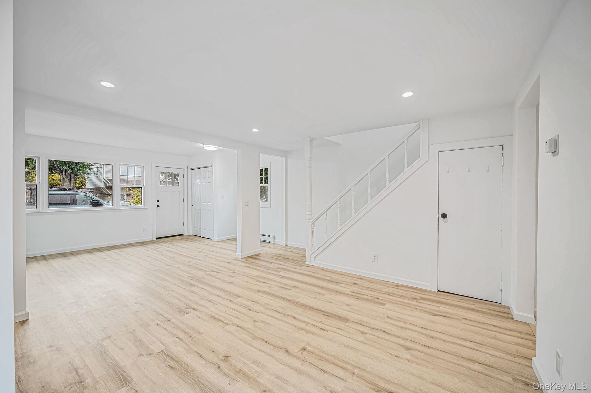 Open-concept interior featuring wood-finish flooring, recessed lighting, and a staircase with white balusters and a decorative post