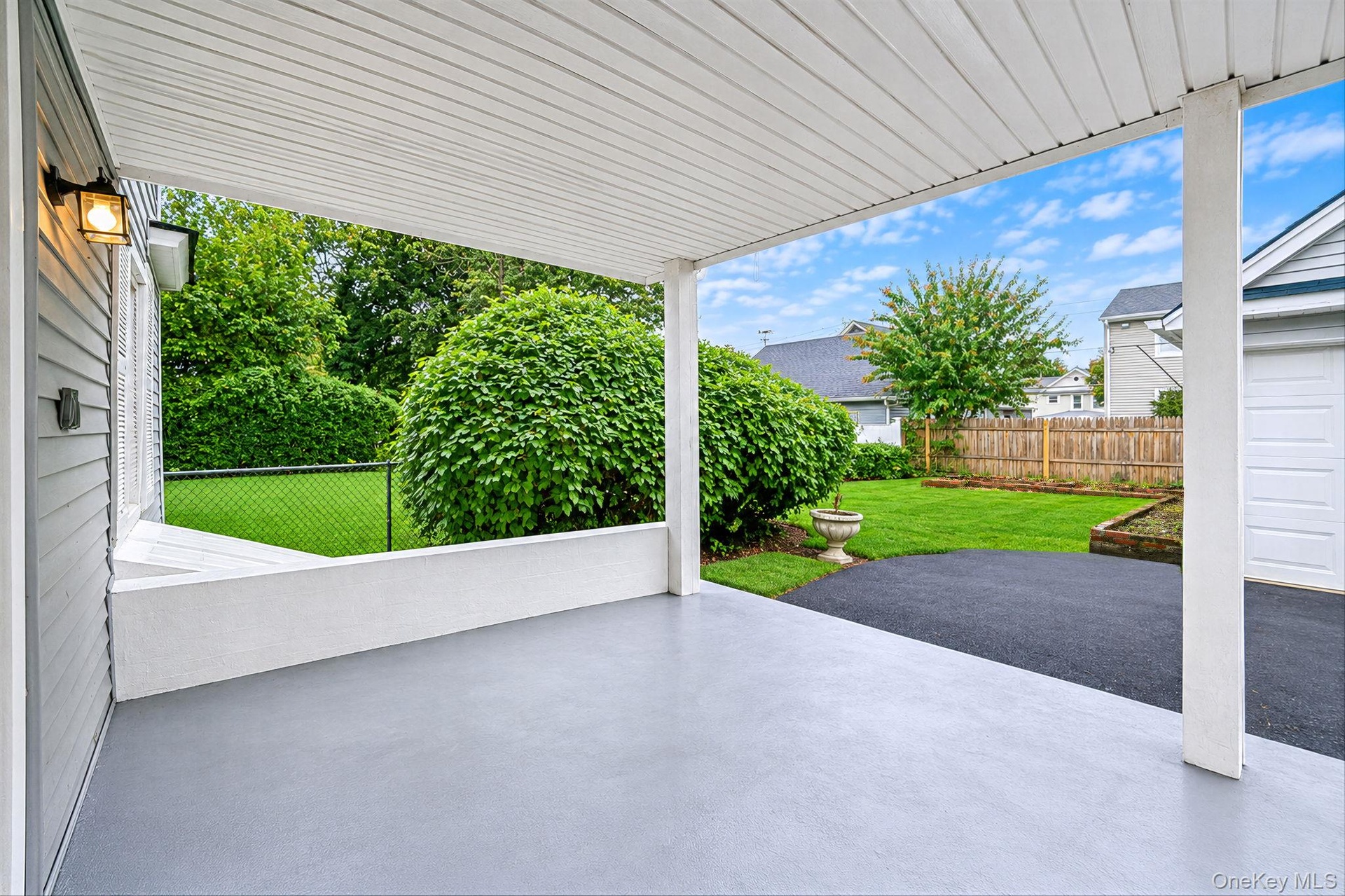 Covered patio featuring a concrete floor, beadboard ceiling, wall-mounted exterior light fixture, and low-profile masonry wall, opening to a fenced ba
