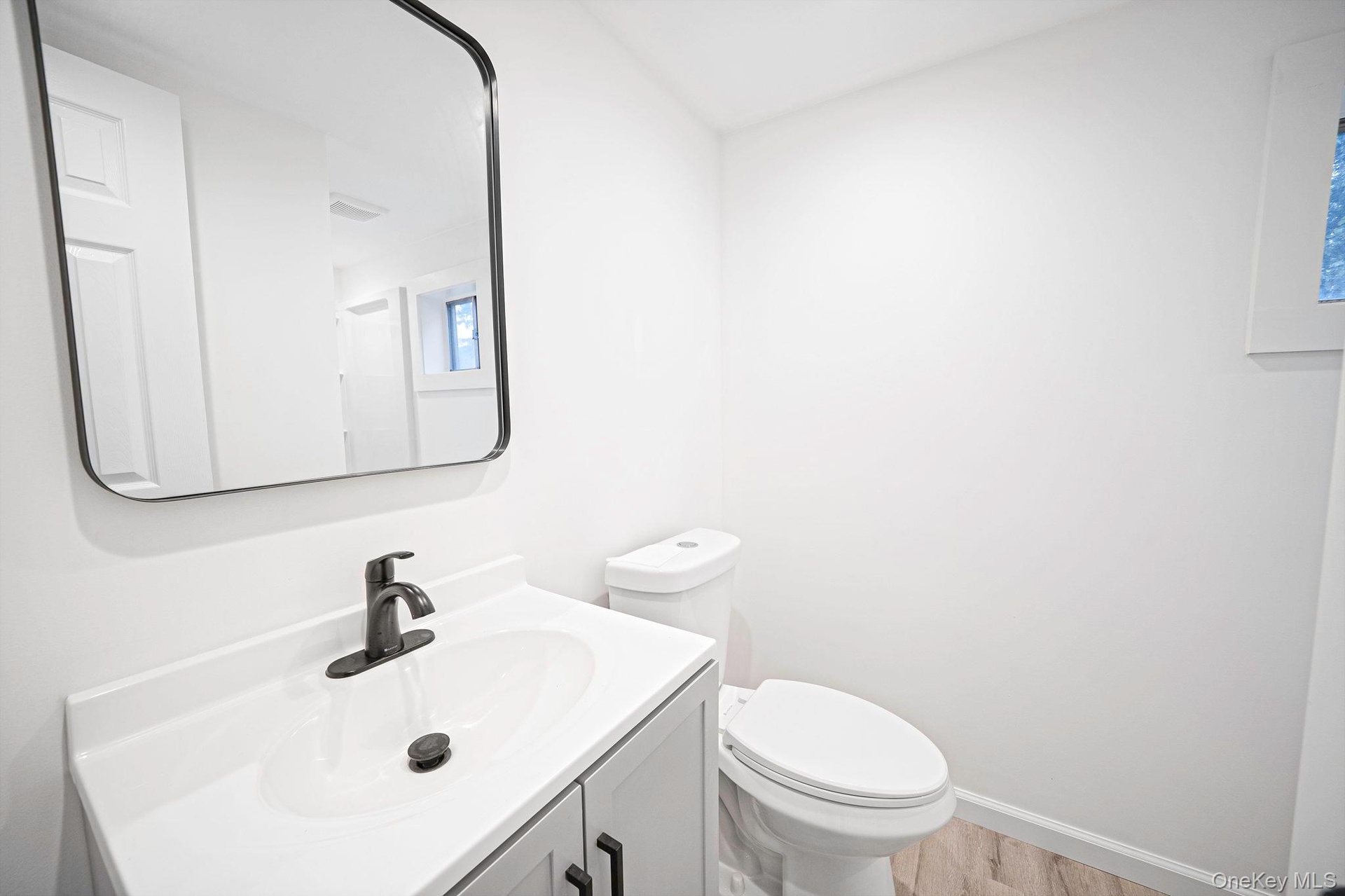 First floor bathroom featuring a grey vanity cabinet with a white countertop, oval basin, matte black faucet, and a rectangular mirror with a rounded 