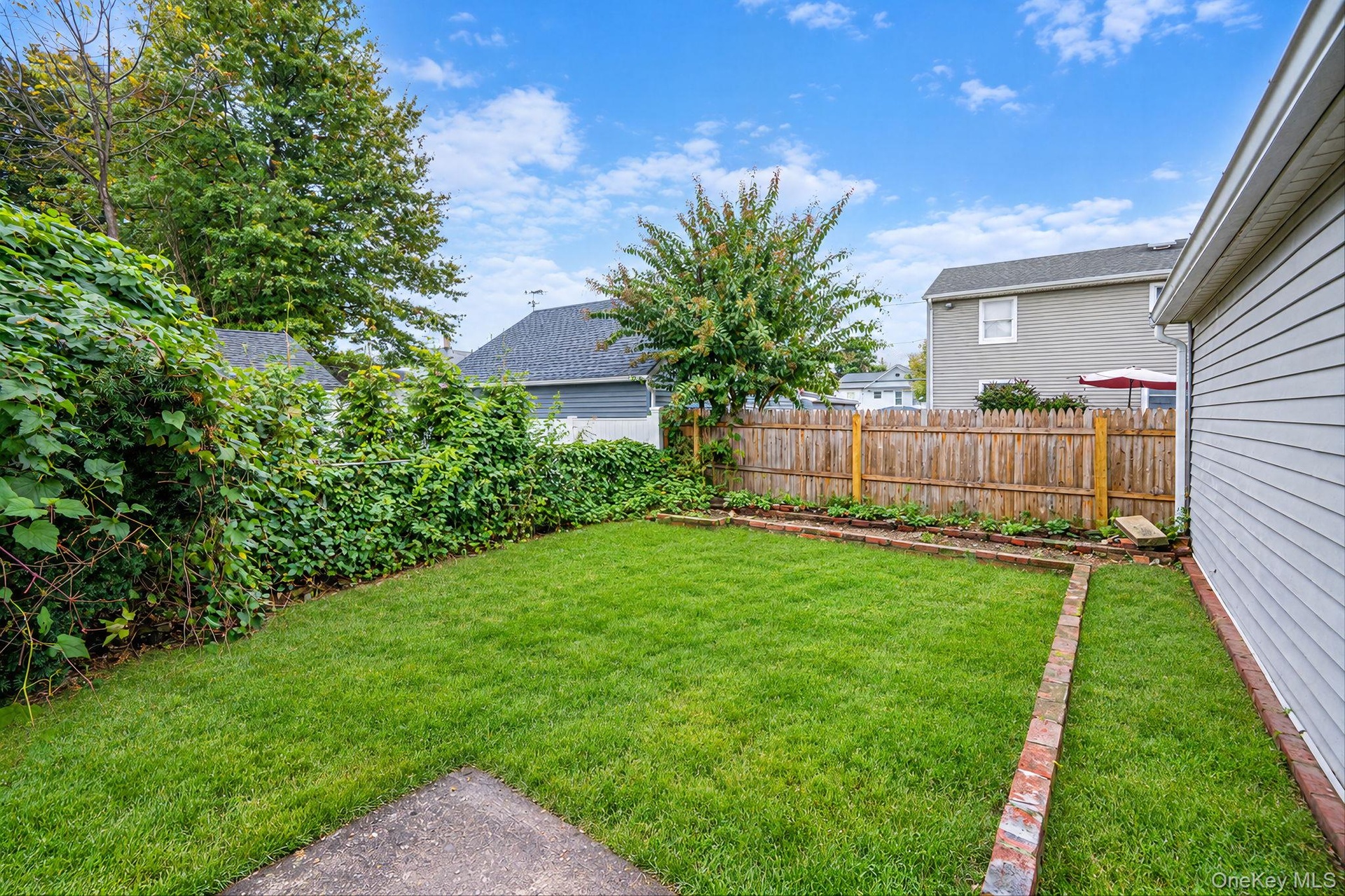 Private backyard featuring a fenced perimeter, brick-edged garden beds, and mature landscaping *virtually edited