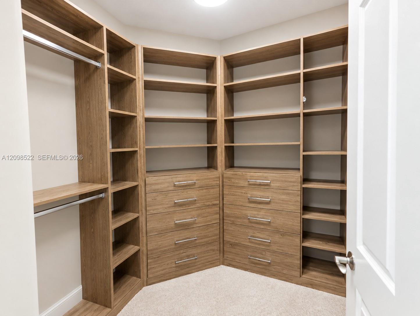 Walk-in closet featuring custom wood-finish built-in shelving, multiple integrated storage drawers, brushed metal hardware, and hanging rods