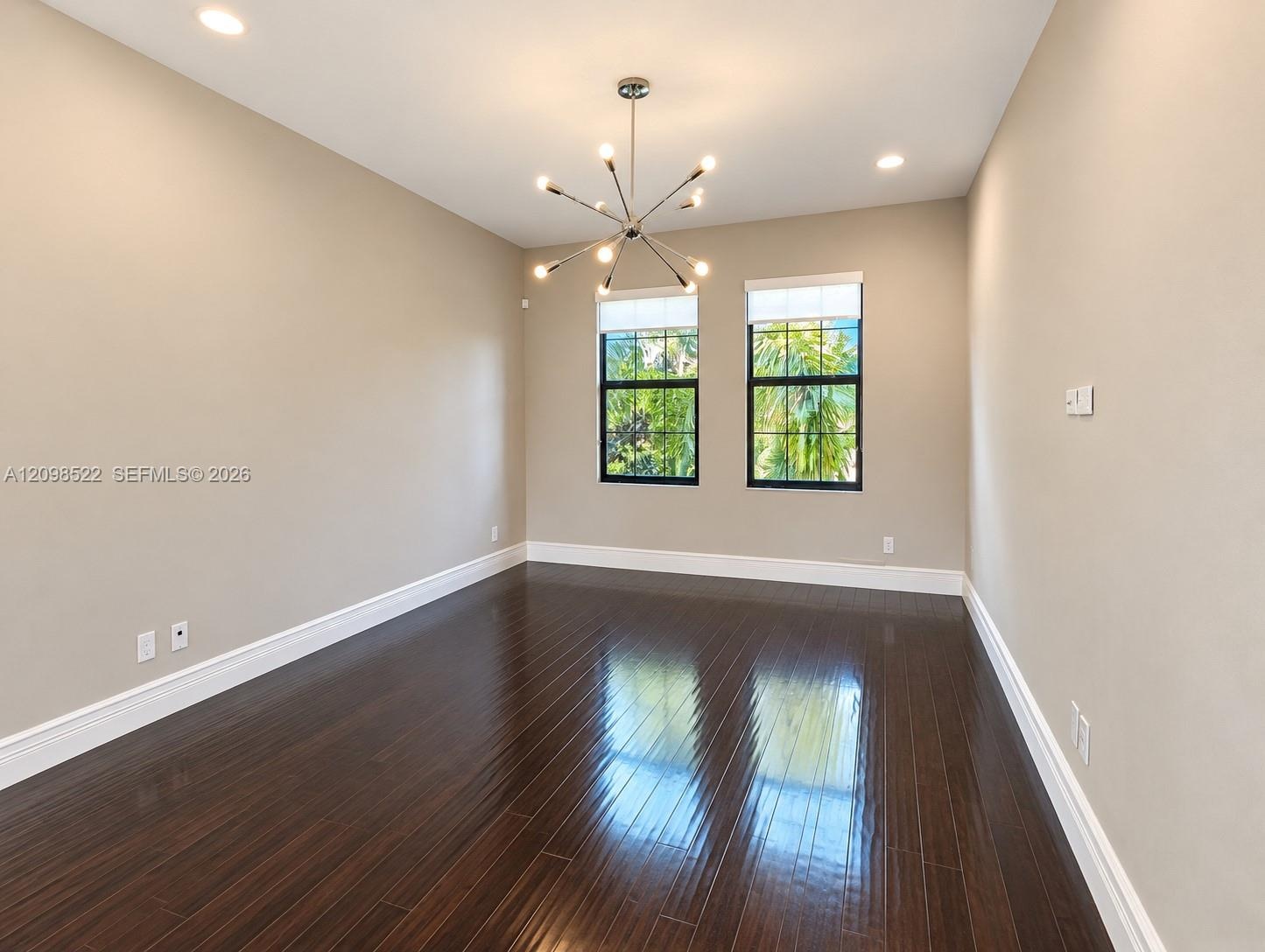 Dark wood-finish flooring, recessed lighting, and a multi-arm polished metal chandelier, featuring dual windows with black frames