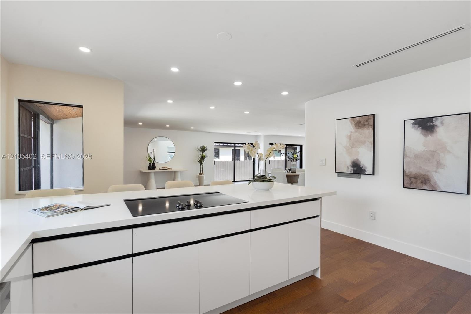 Kitchen island featuring white flat-panel cabinetry, a solid surface countertop, and an integrated cooktop, complemented by recessed lighting and wood