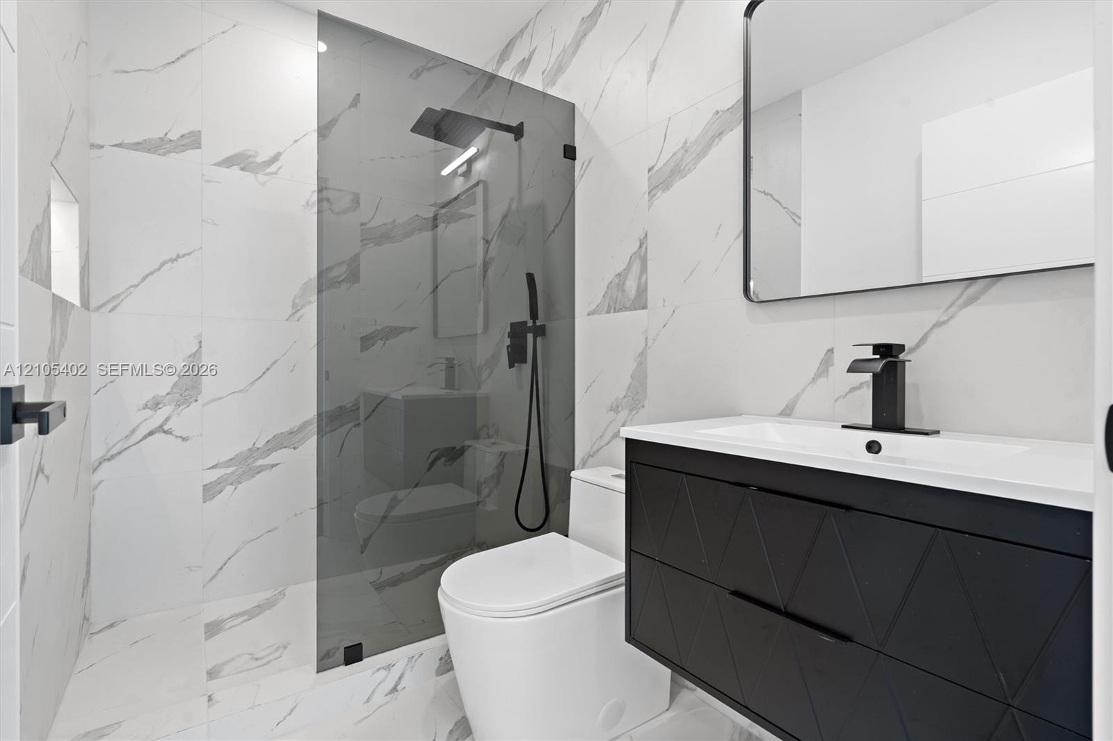 Modern bathroom featuring large-format wall and floor tile with a veined pattern, walk-in shower with glass panel, matte black plumbing fixtures, and 