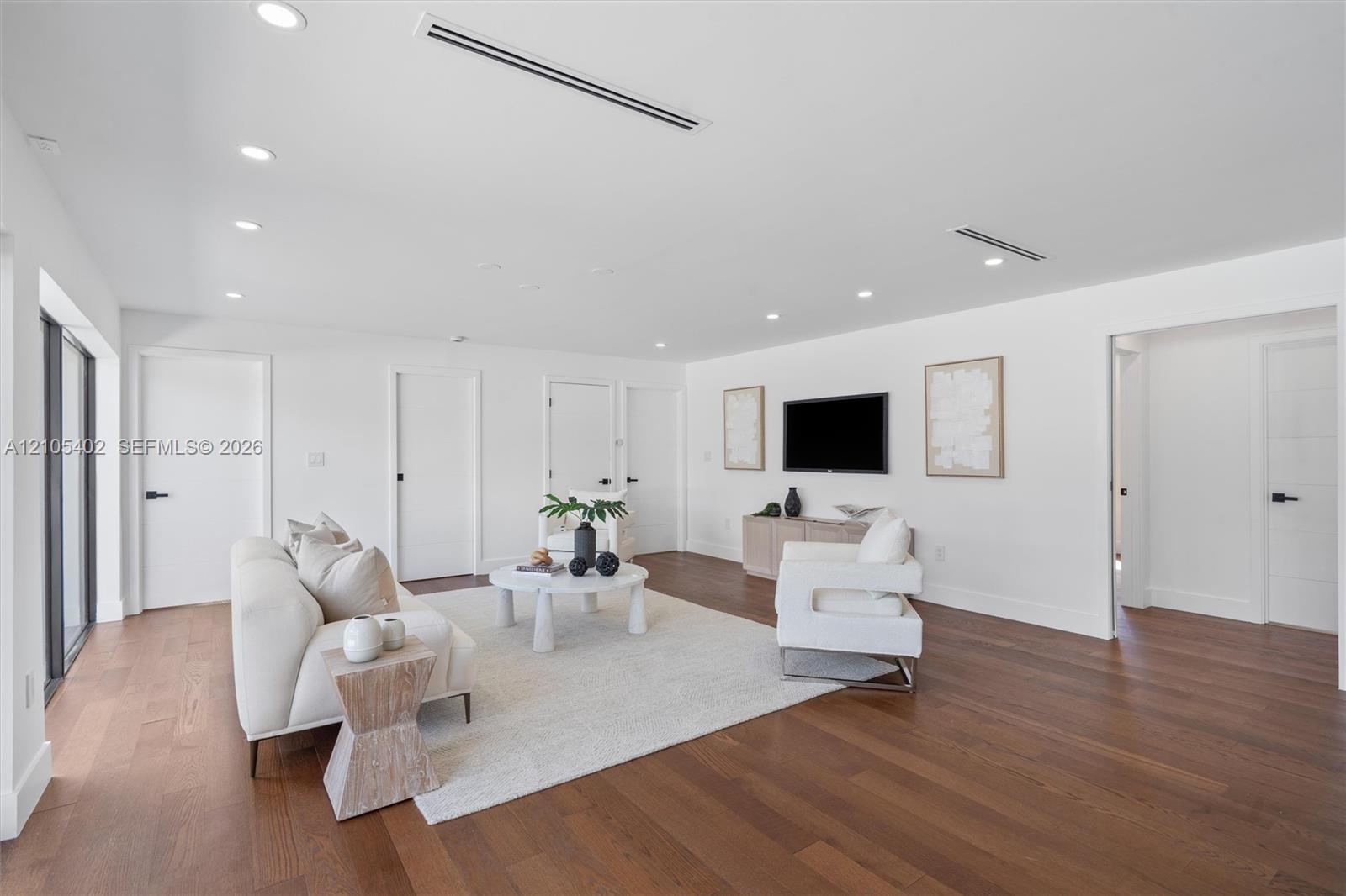 Open-concept interior featuring wood-finish flooring, recessed lighting, linear HVAC diffusers, and solid-core doors with matte black hardware
