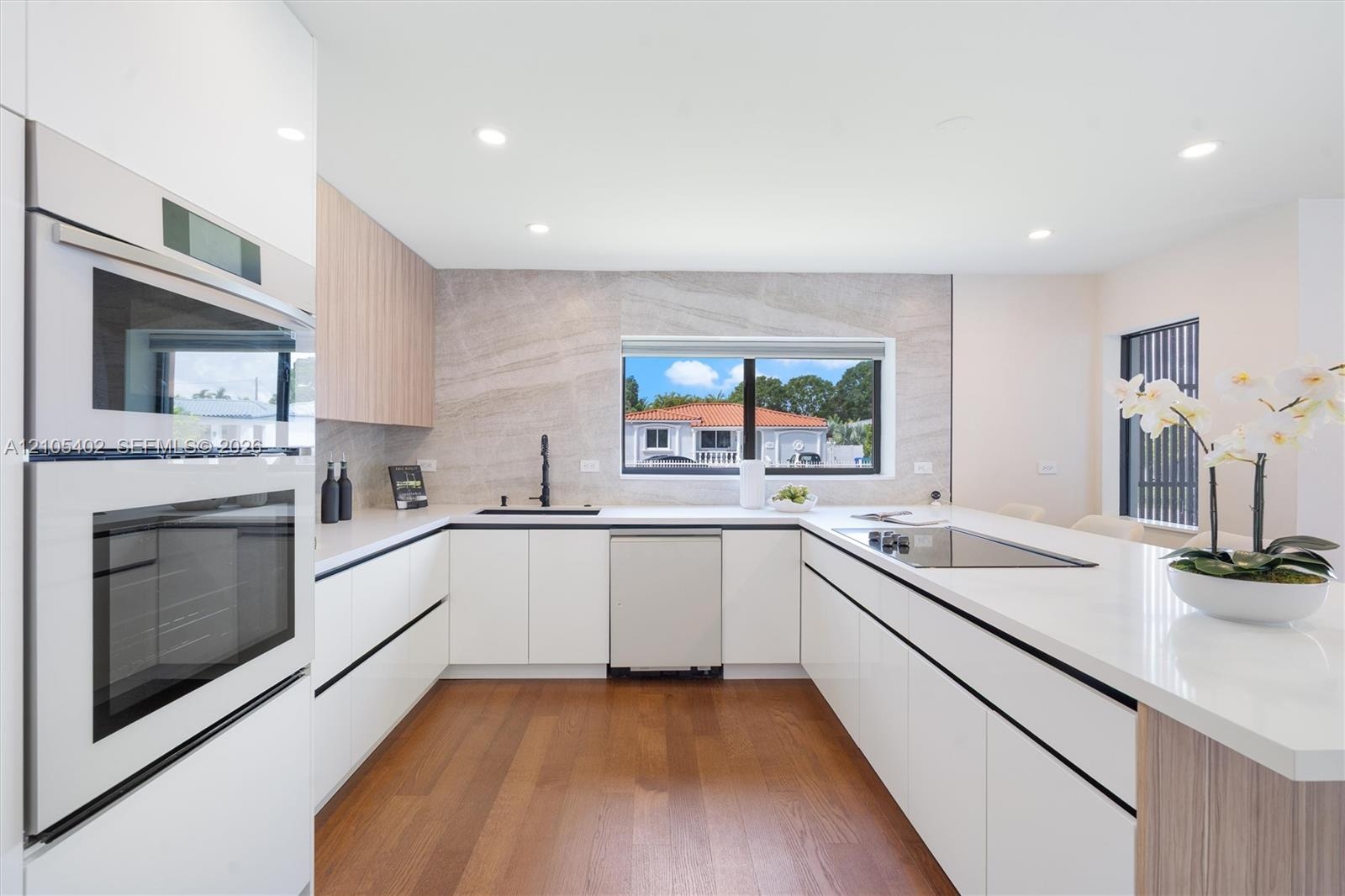 Modern kitchen featuring white flat-panel cabinetry, wood-finish cabinetry accents, quartz countertops, a stone-patterned backsplash, and integrated s