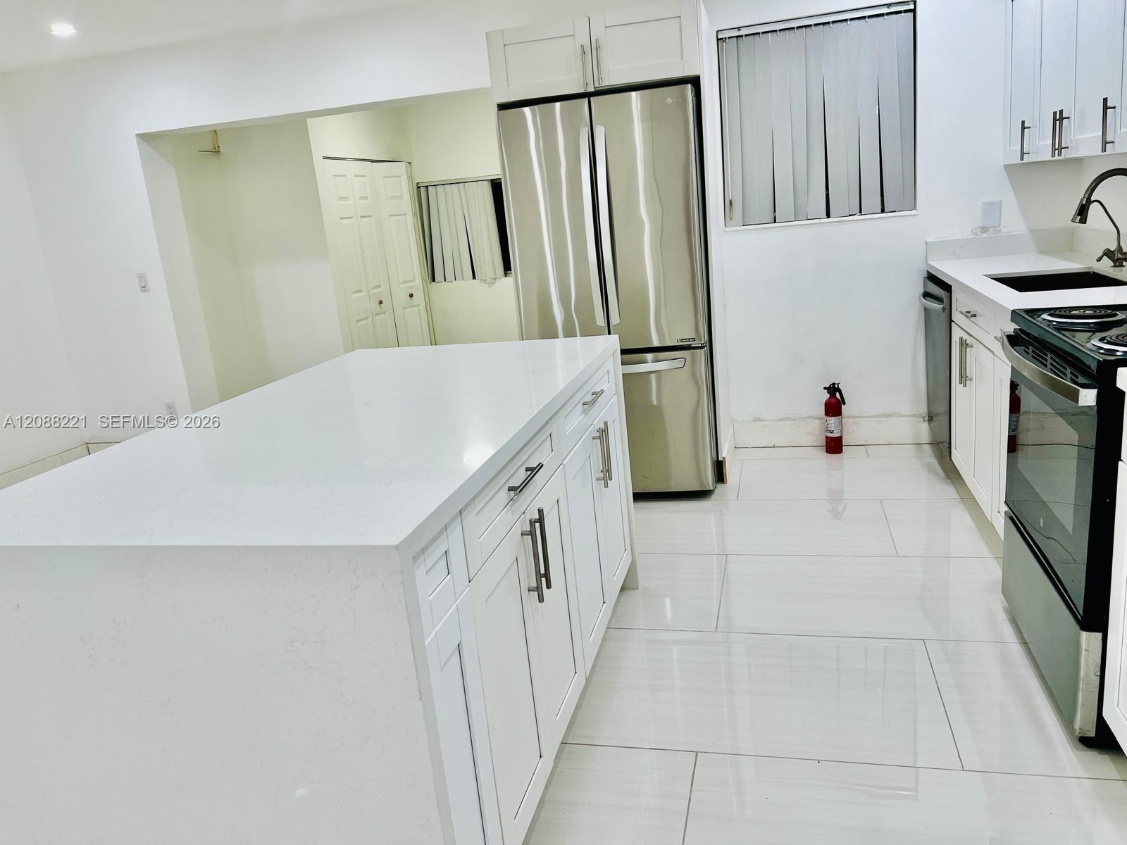 Kitchen featuring white cabinetry, an island with a solid surface countertop, stainless steel appliances, and large-format tile flooring throughout