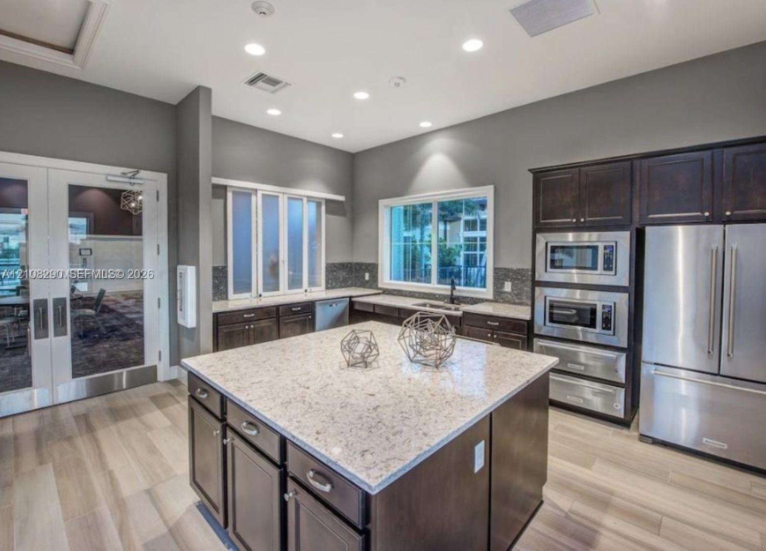 Kitchen featuring a central island with a stone countertop, dark wood cabinetry, stainless steel built-in appliances, recessed lighting, and wood-fini