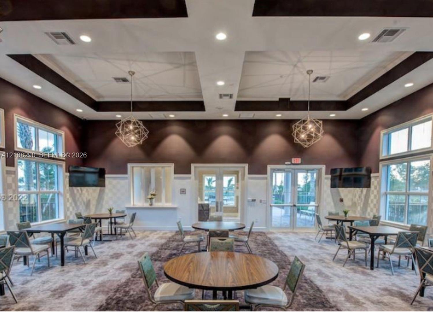 Coffered ceiling with dark accent trim, recessed lighting, dual geometric metal chandeliers, extensive wall-to-wall windows, and double glass-panel en
