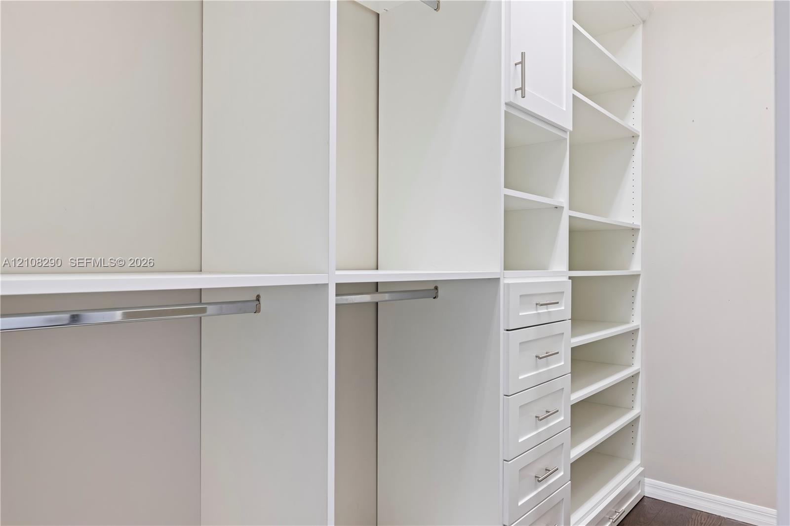 Custom closet featuring floor-to-ceiling white cabinetry, built-in shelving, integrated hanging rods, and a bank of storage drawers with brushed metal
