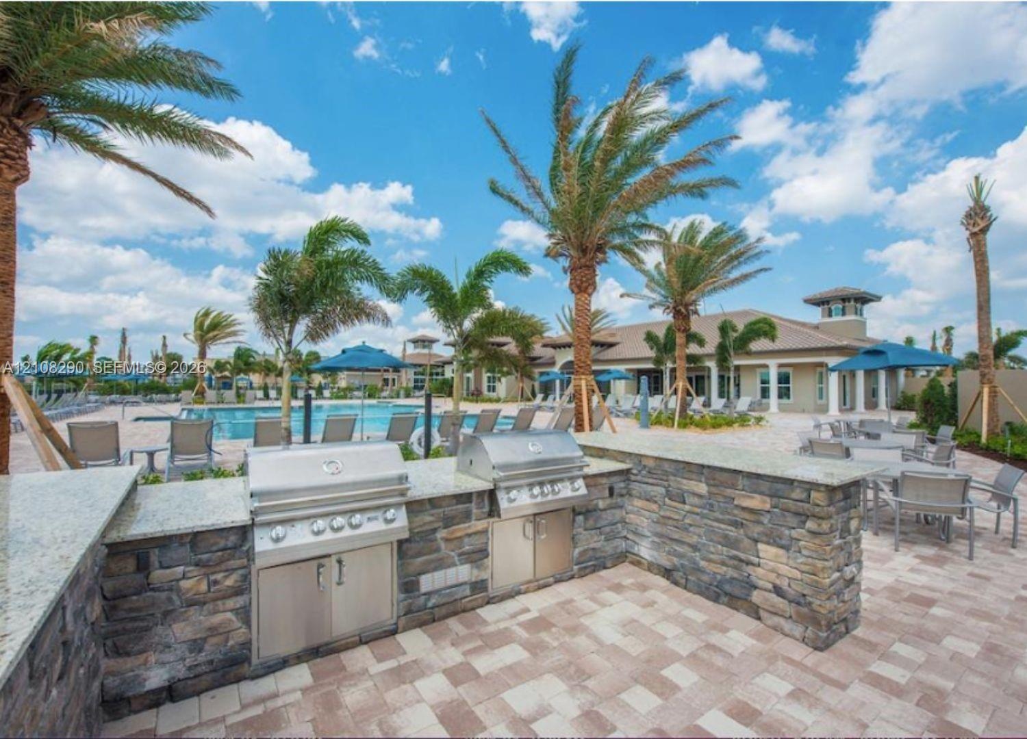 Outdoor kitchen featuring dual stainless steel built-in grills, stone veneer facade, and expansive light-toned countertop surfaces