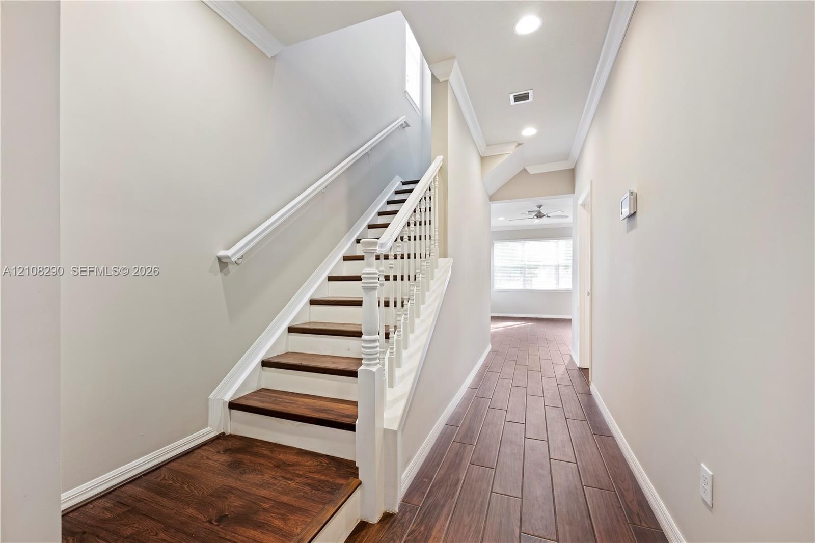 Interior hallway featuring wood-finish flooring, staircase with white spindle railings, wood-toned treads, and recessed lighting