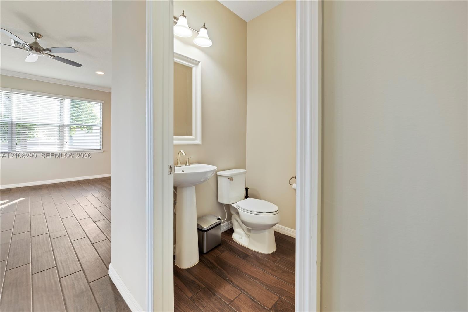 Pedestal sink with a polished metal faucet, multi-light fixture, white toilet, and wood-finish tile flooring