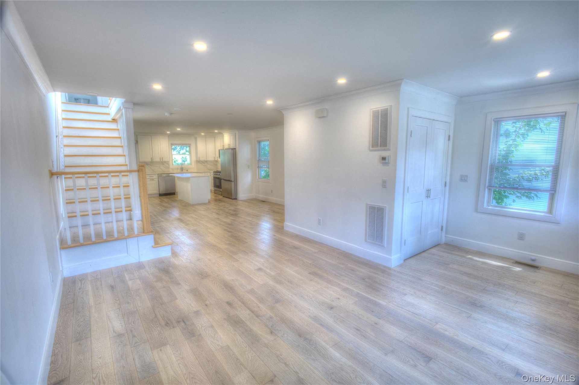 Open-concept living space featuring wood-finish flooring, recessed lighting, a staircase with white balusters and a wood handrail, and white kitchen c