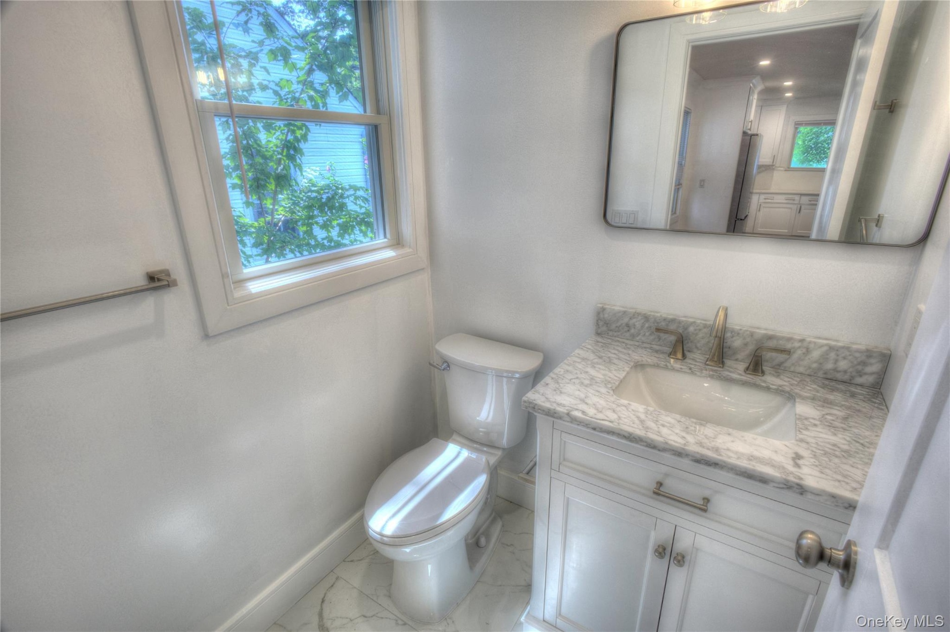 Vanity featuring a stone-patterned countertop, integrated basin with metal hardware, white cabinetry, rectangular wall mirror, and large-format tile f