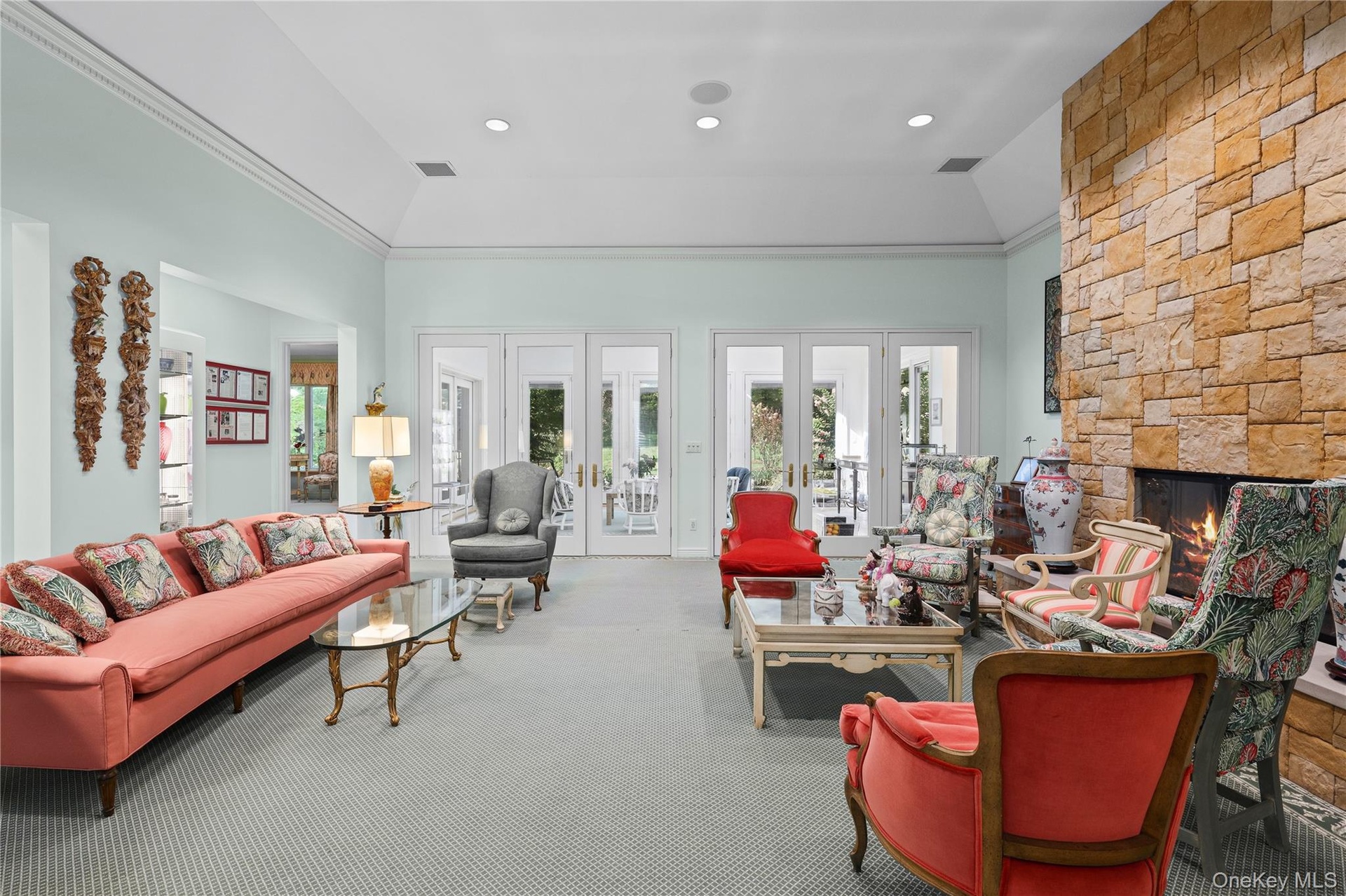 Living area featuring a floor-to-ceiling natural stone fireplace, vaulted ceilings, crown molding, recessed lighting, and multiple sets of glass-paned