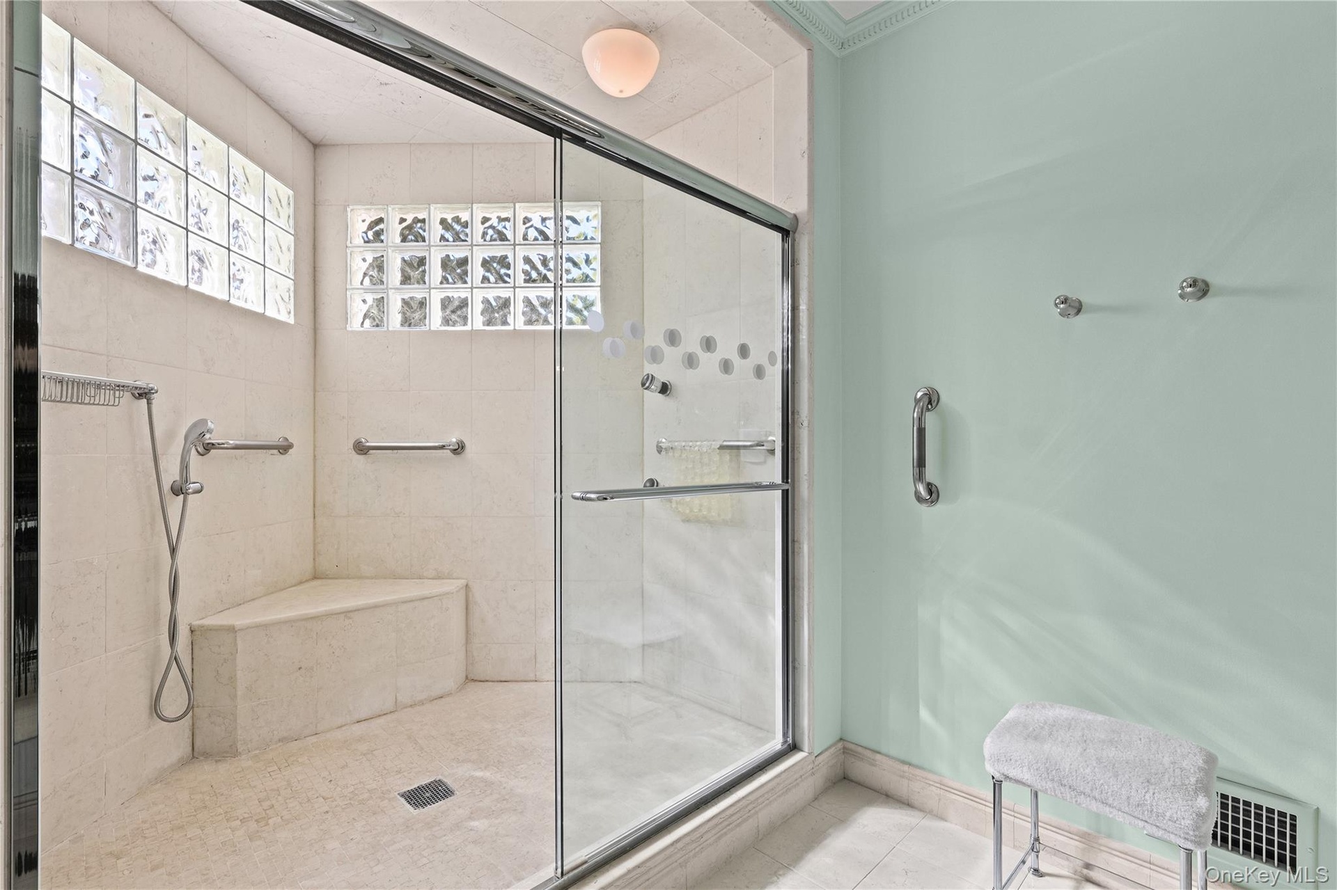 Walk-in shower featuring natural stone tiling, a built-in bench seat, glass block windows, and a semi-frameless glass enclosure