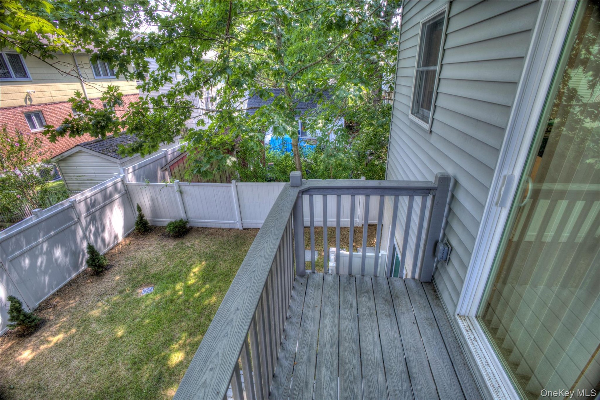 Elevated deck featuring wood-finish decking and vertical railings, overlooking a fenced backyard with a manicured lawn and mature trees