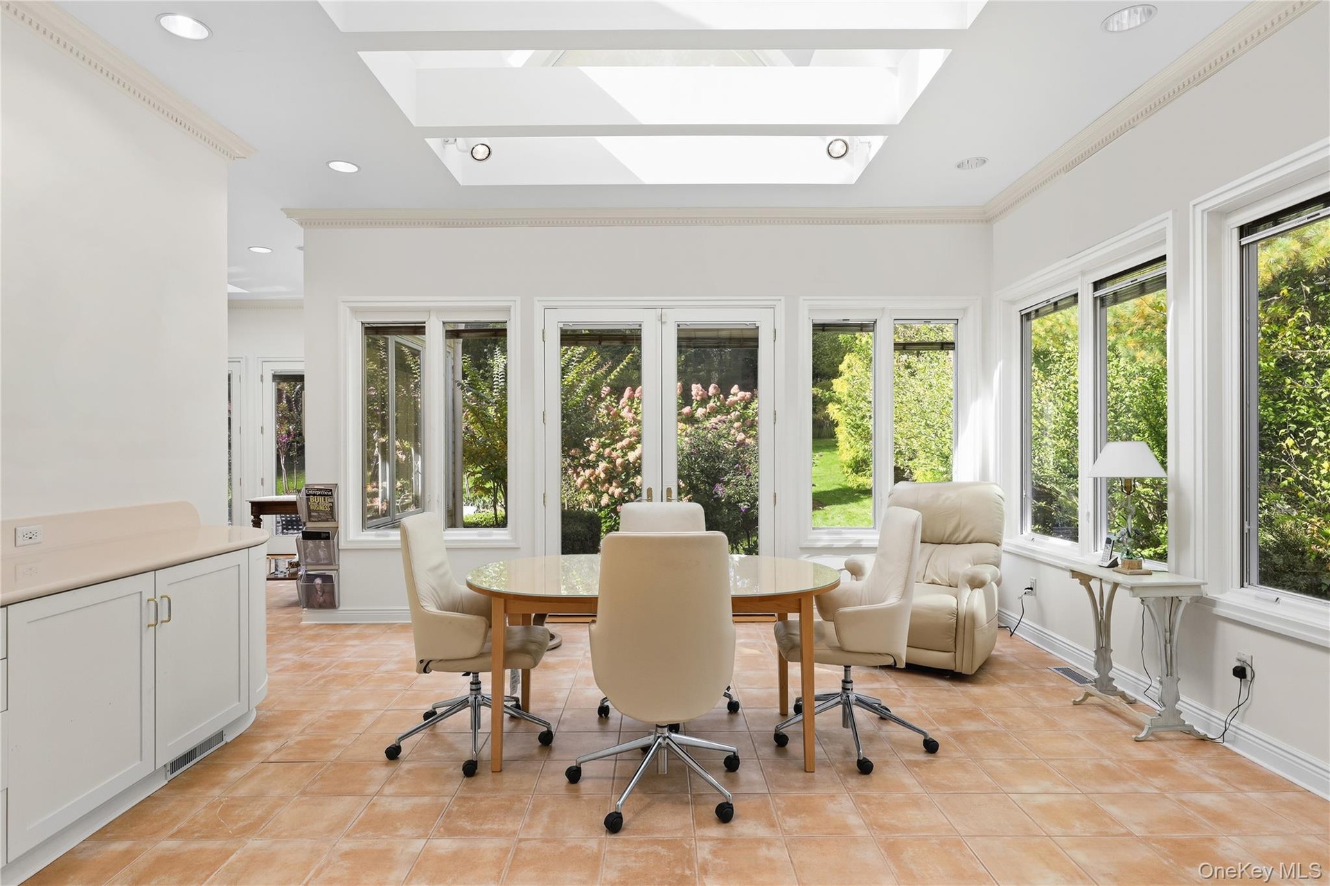 Sunroom featuring a vaulted ceiling with large skylights, tile flooring, built-in cabinetry with solid-surface countertop, and extensive multi-pane wi