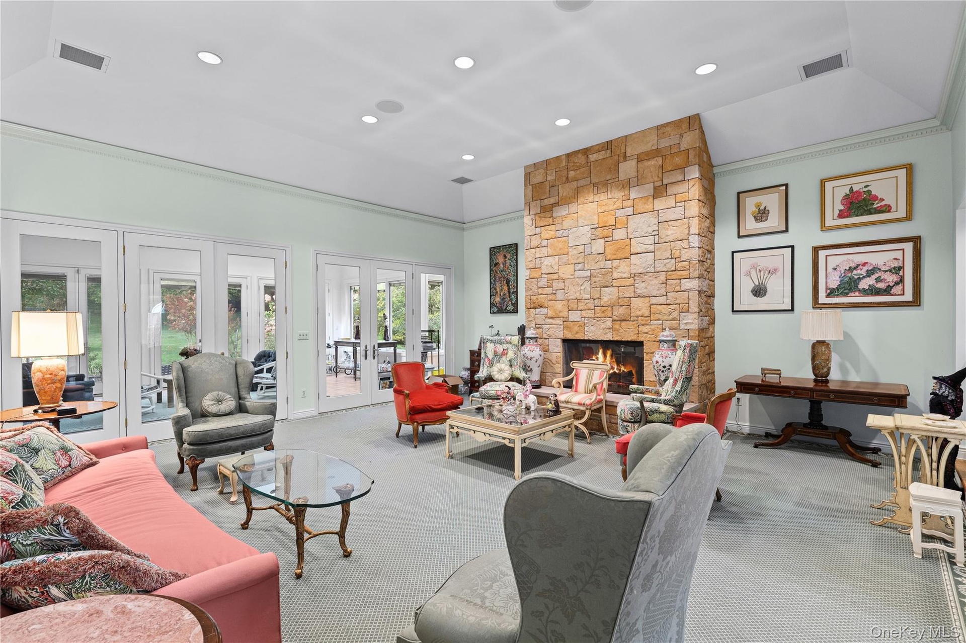 Vaulted ceiling with recessed lighting, stone fireplace, and multiple sets of glass-paned double doors
