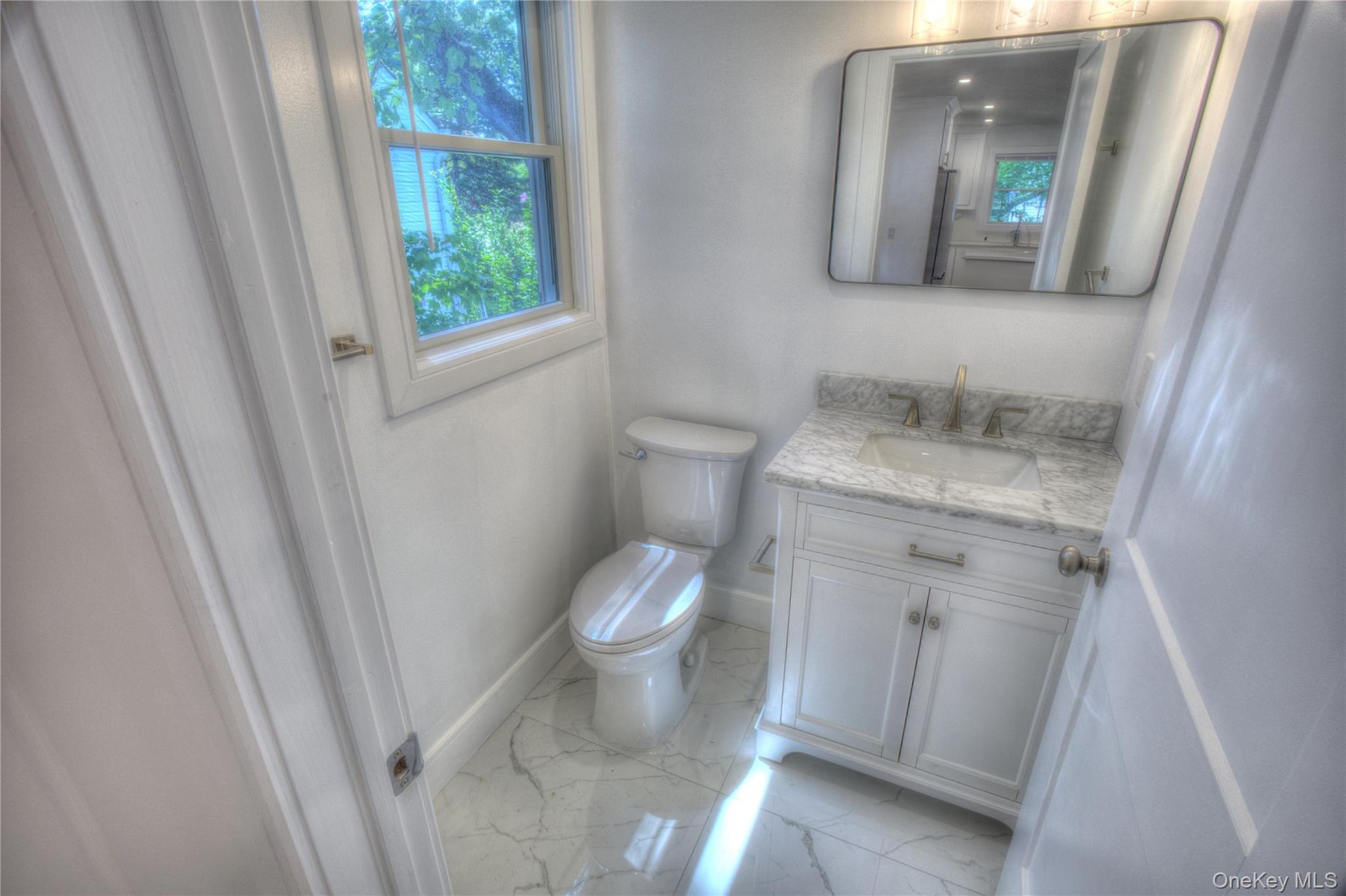 White cabinetry vanity with stone-composite countertop, undermount sink, metallic faucet, rectangular wall-mounted mirror, and stone-patterned tile fl