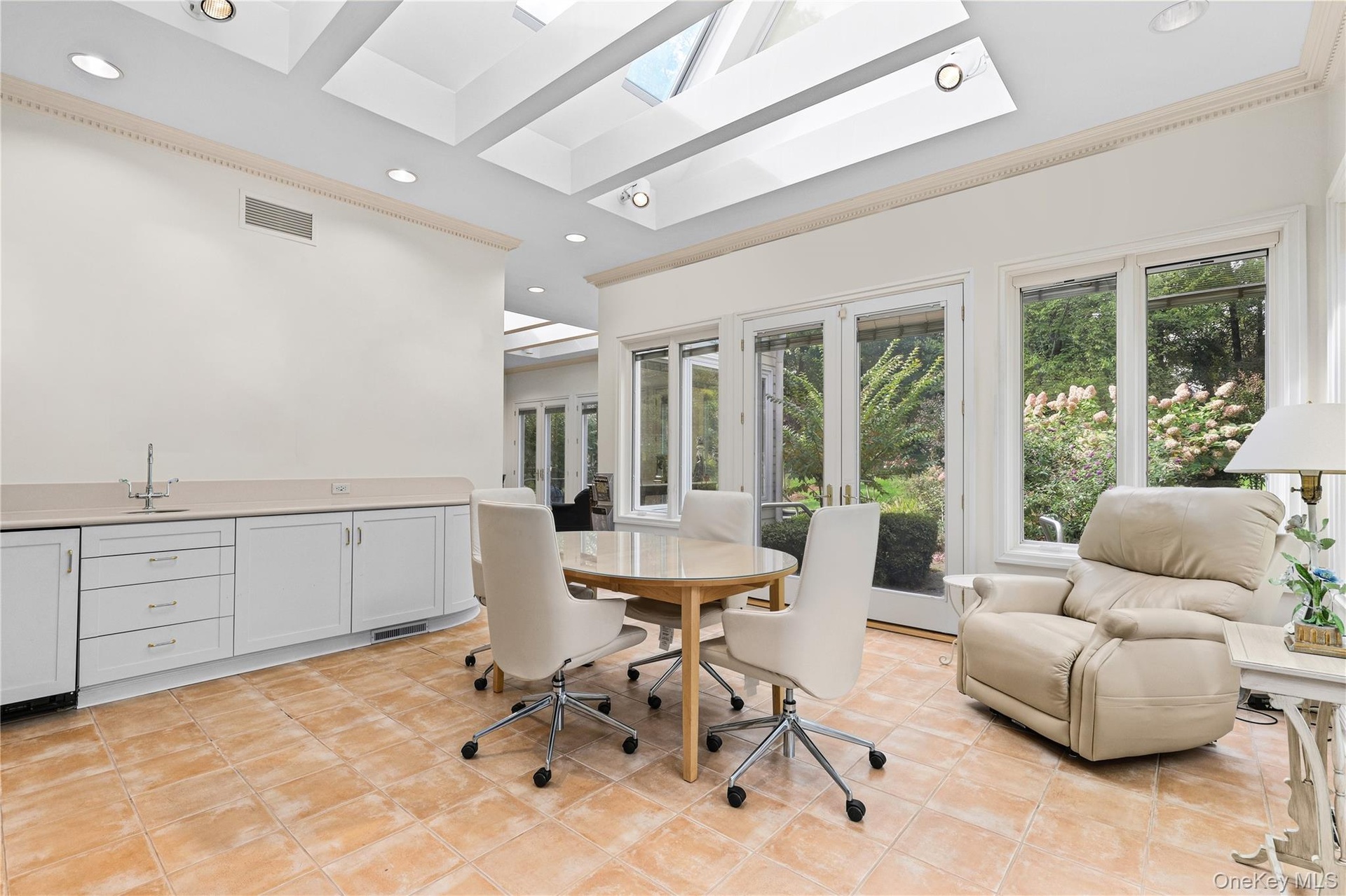 Sunroom featuring vaulted ceilings with skylights, tile flooring, built-in cabinetry with a sink, and double glass doors