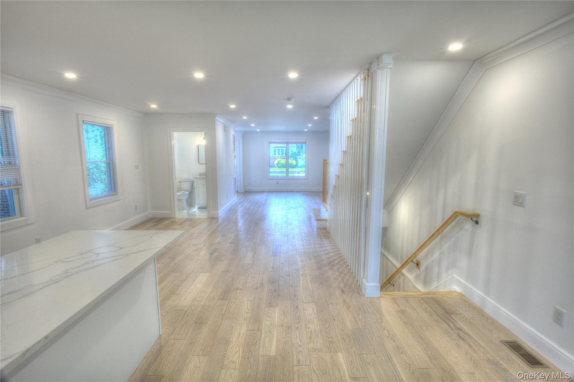 Open-concept interior featuring wood-finish flooring, recessed lighting, a stone-topped kitchen island, and a wooden handrail with vertical balusters