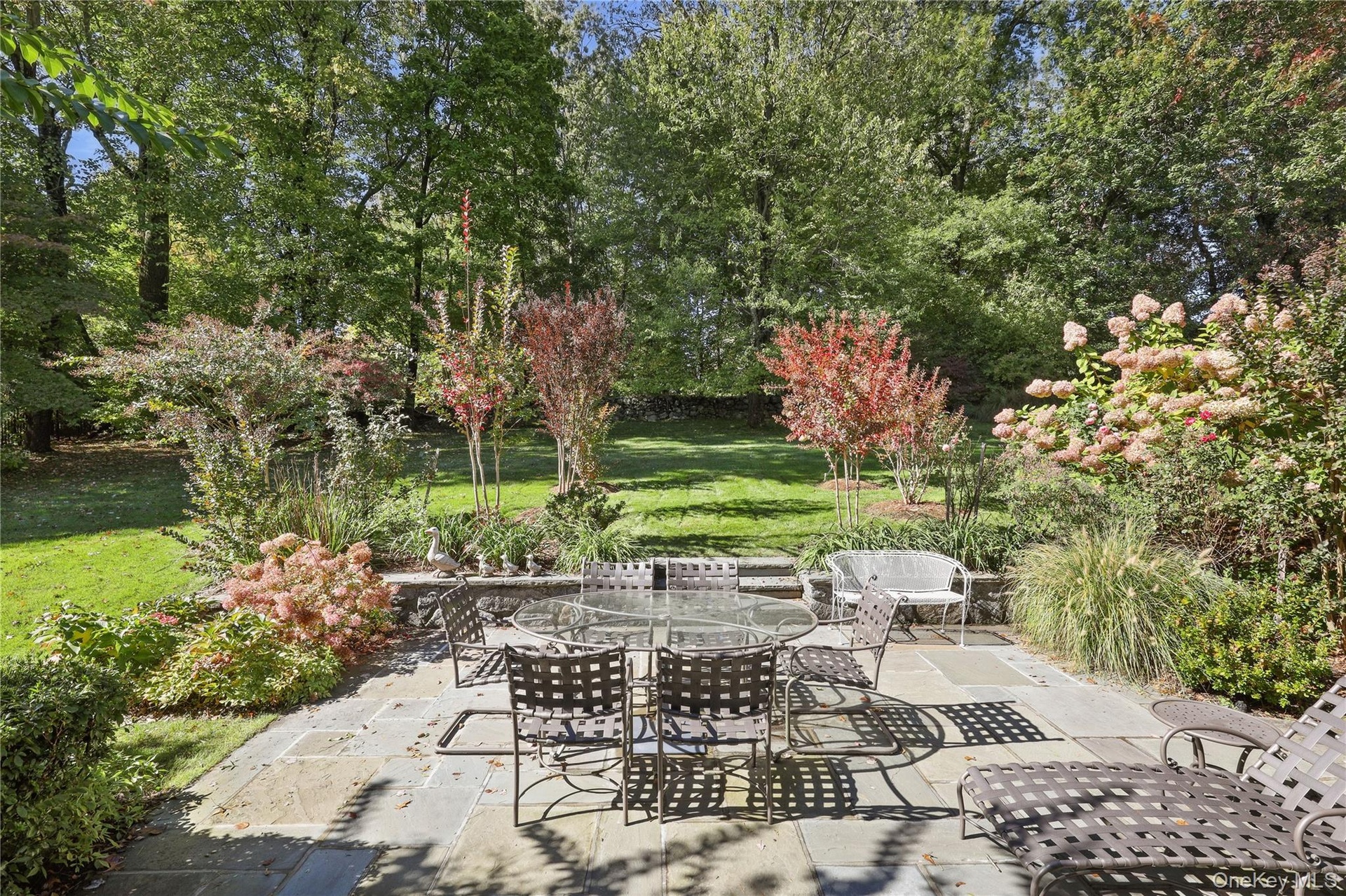 Flagstone patio featuring a natural stone retaining wall, mature trees, and established landscaping